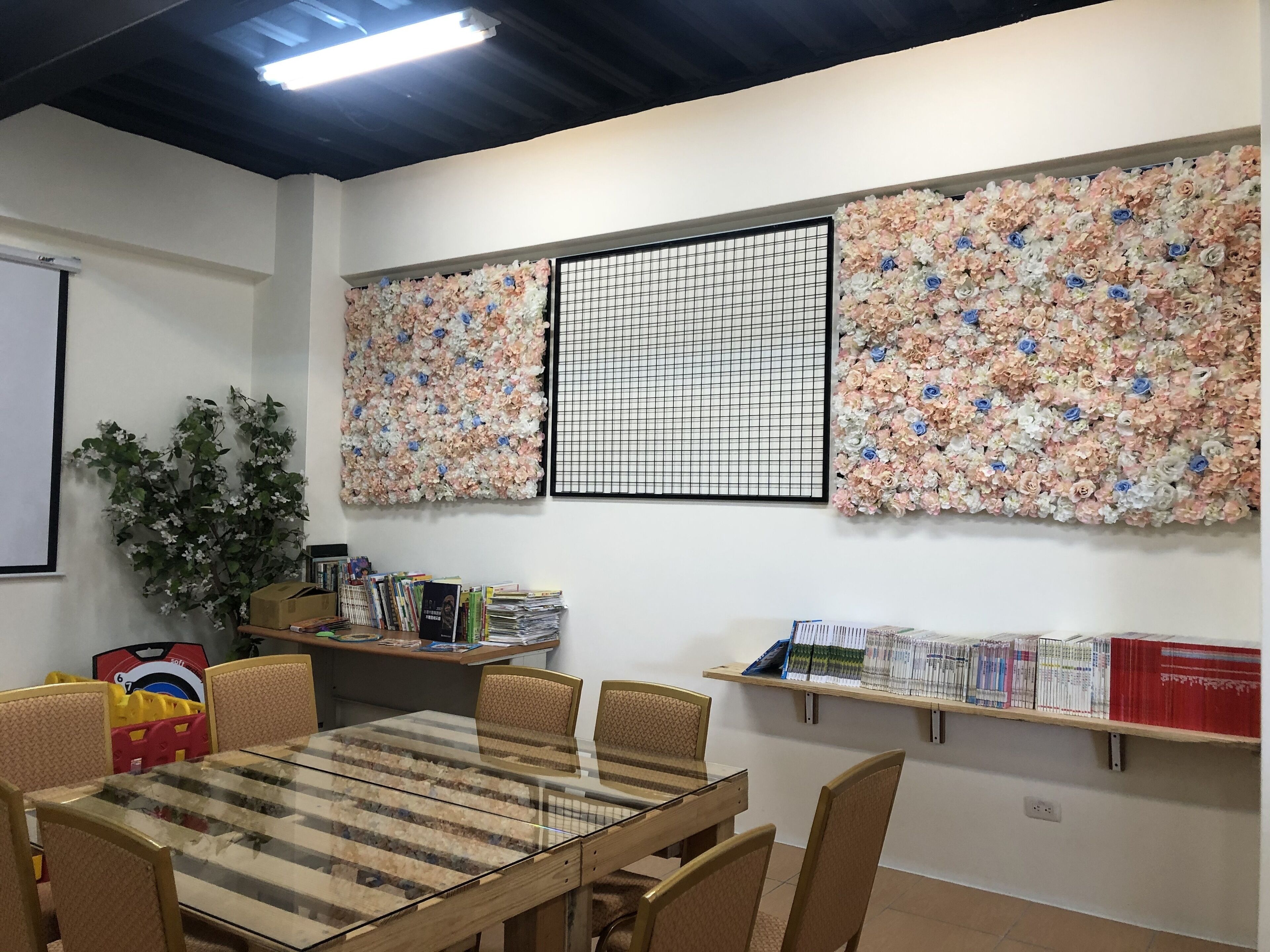 A conference room with a glass table, chairs, a projector screen, and floral wall decorations.