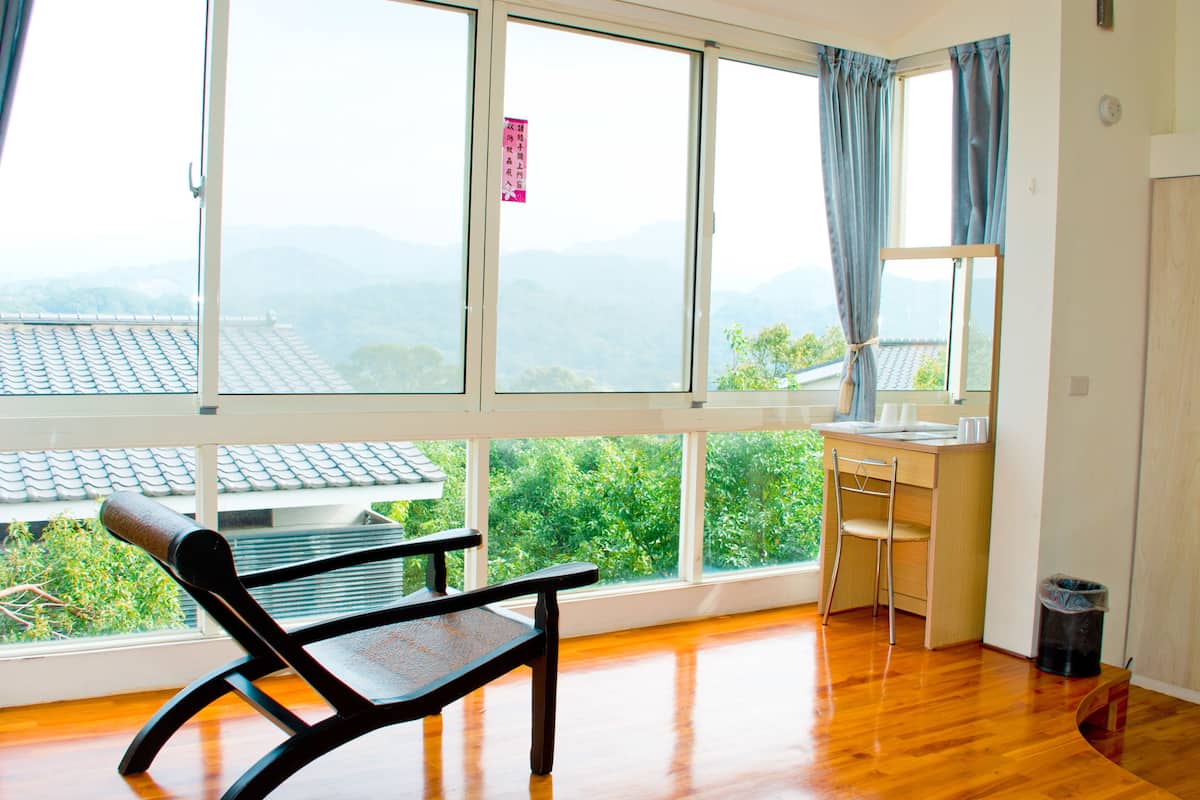 Une pièce dotée d’un plancher en bois, d’un bureau, d’une chaise et de grandes fenêtres donnant sur des collines verdoyantes.