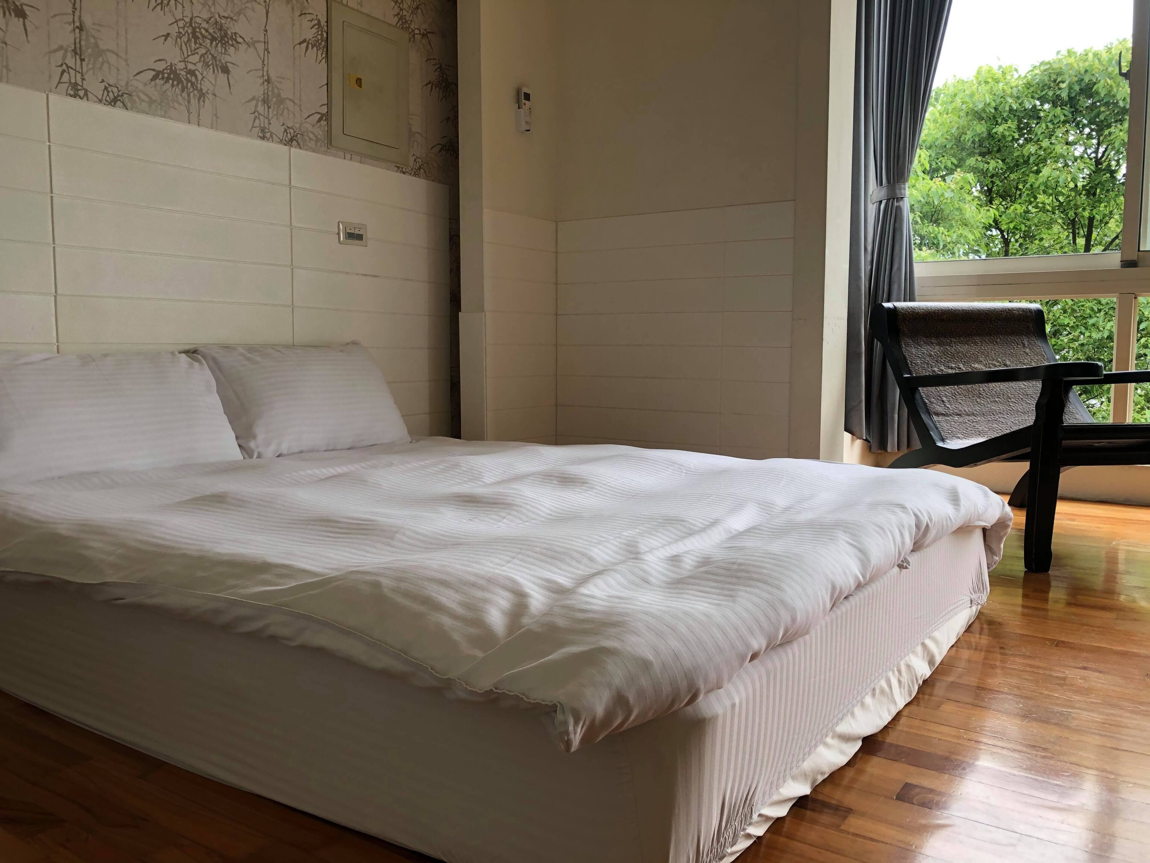 A bedroom with a large bed, a chair, and a window with a view of trees.
