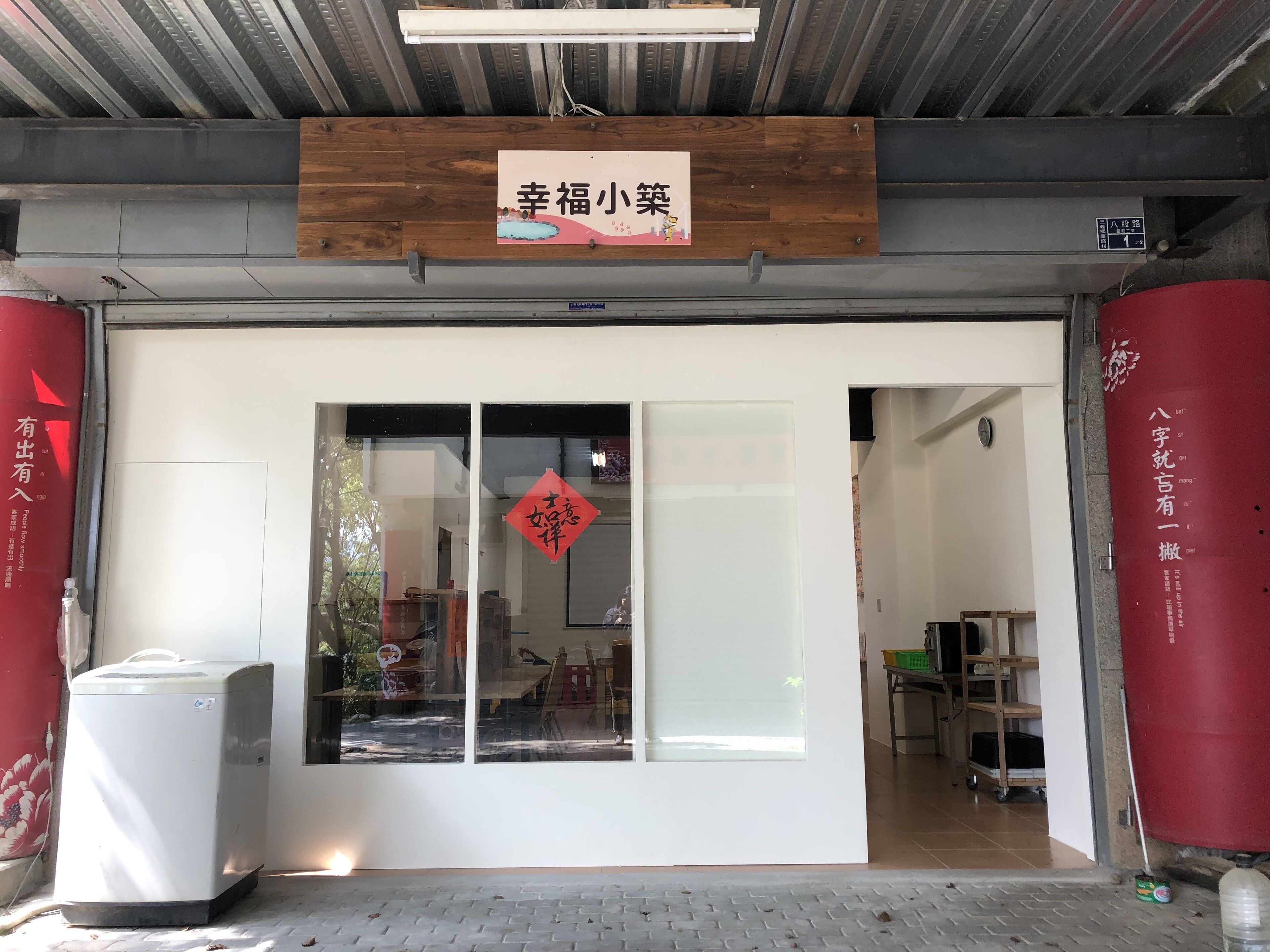 A storefront with a wooden sign above the entrance, a large glass window with a red decoration, and a metal door.