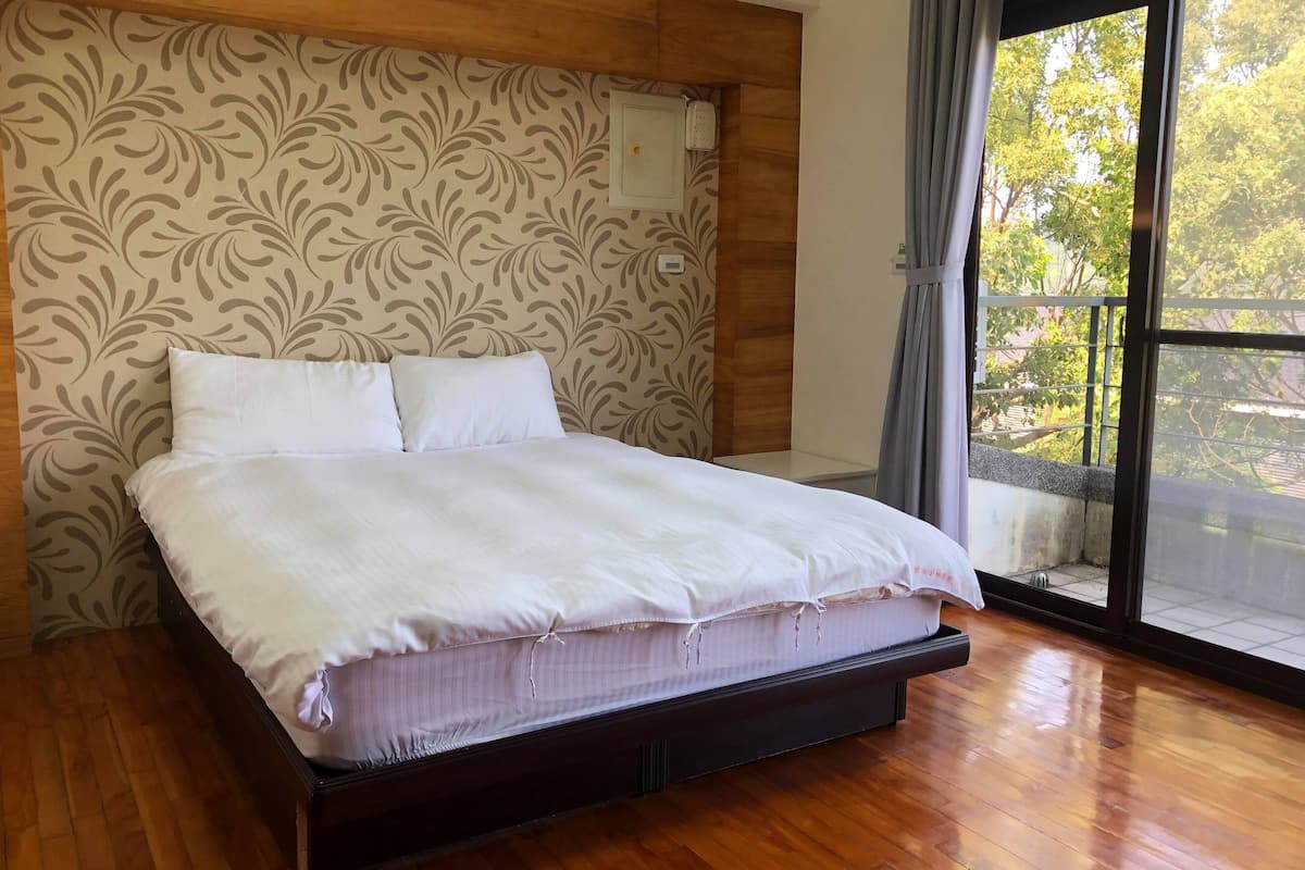 Une chambre à coucher avec une tête de lit en bois, un grand lit avec une literie blanche et une vue sur les arbres par la fenêtre.