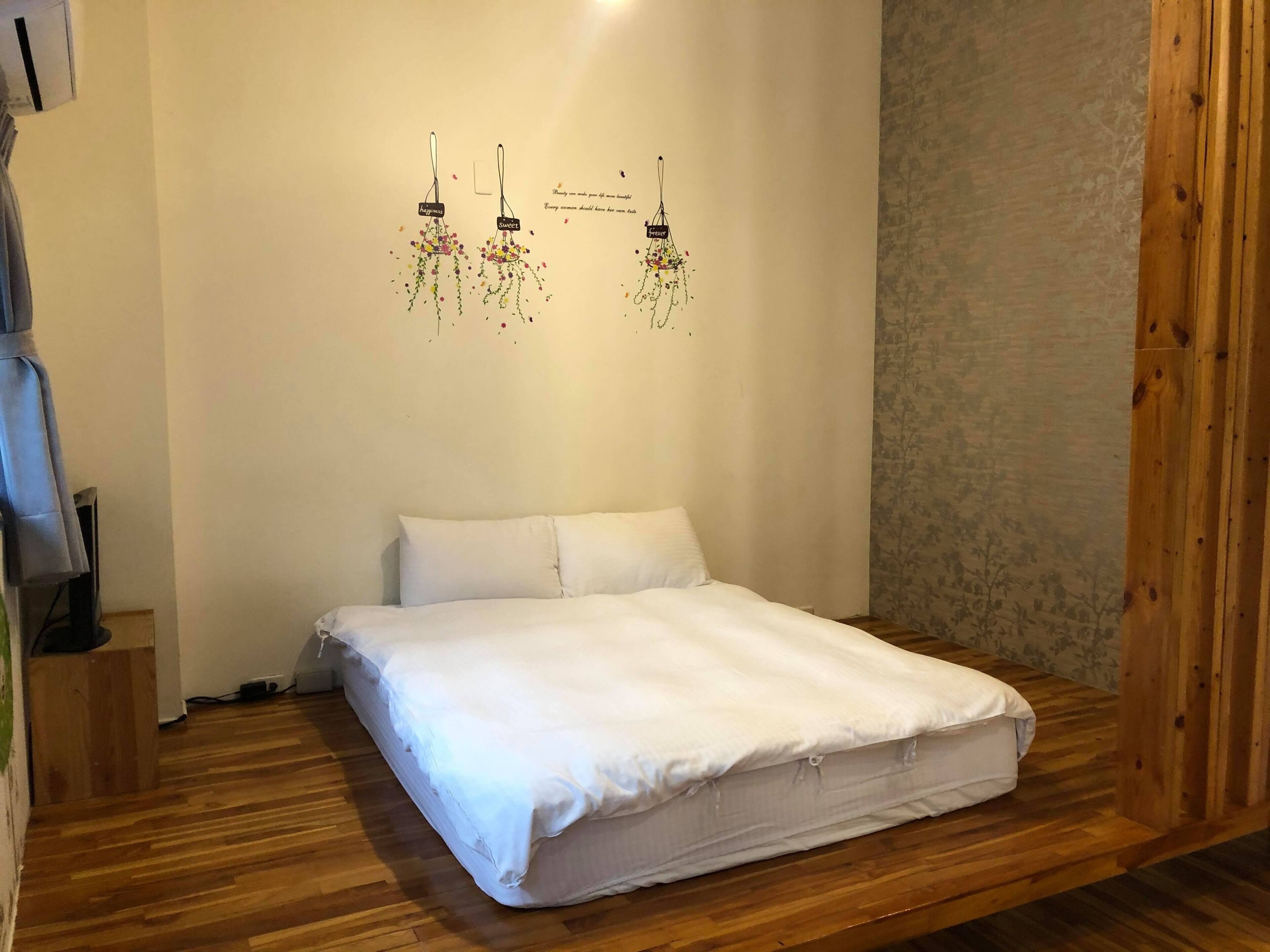 Cama bem arrumada com roupa de cama branca em quarto com piso de madeira e parede lisa.