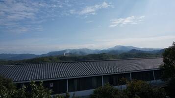 A building with a tiled roof, surrounded by greenery and mountains in the background.