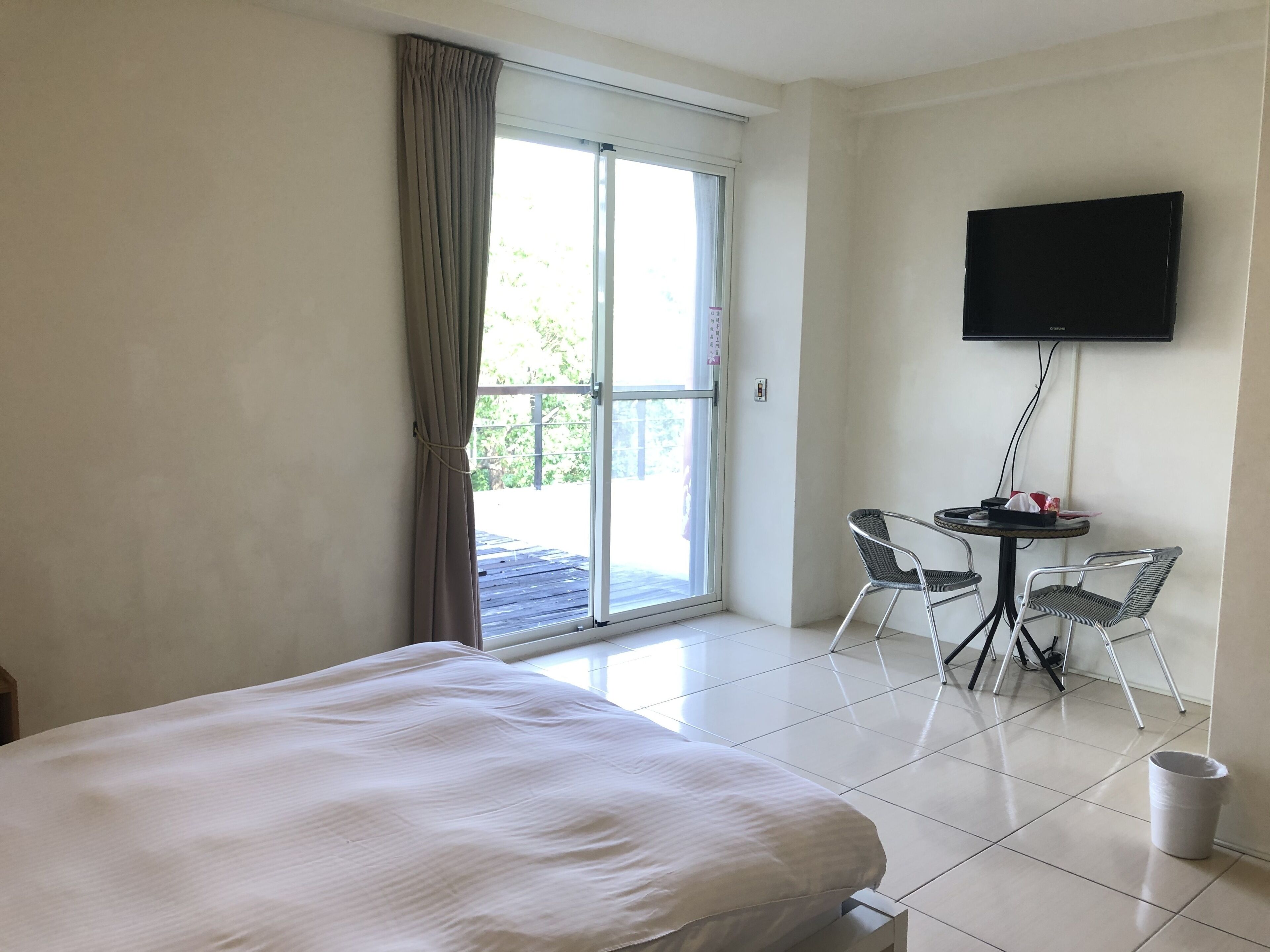 Een hotelkamer met een bed, een tafel met stoelen, een televisie en een schuifdeur naar buiten.