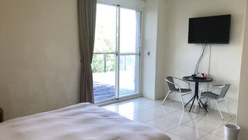 Een hotelkamer met een bed, een tafel met stoelen, een televisie en een schuifdeur naar buiten.