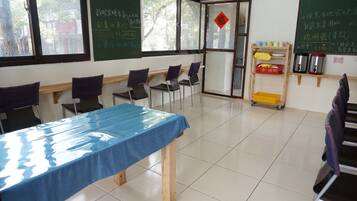 A classroom with a blue table, chairs, a chalkboard, and a window with a view of trees.