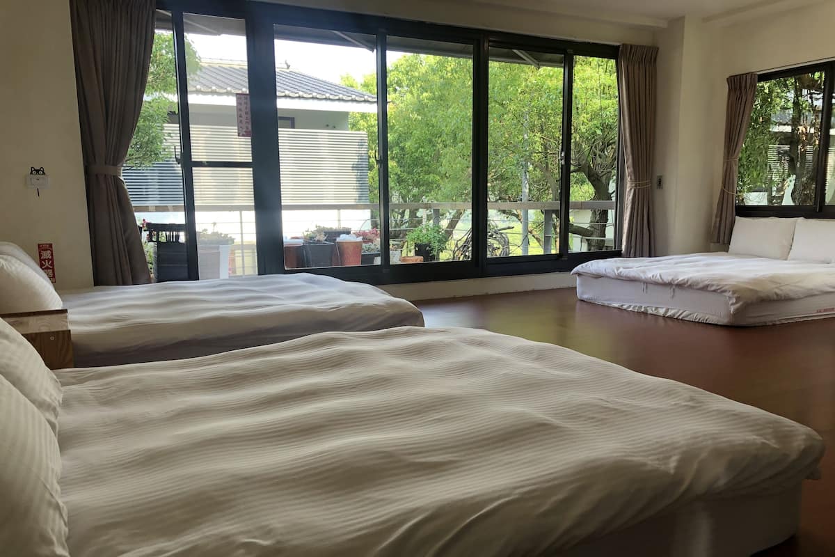 Une chambre d’hôtel avec deux lits, de grandes fenêtres et une vue sur la verdure environnante.