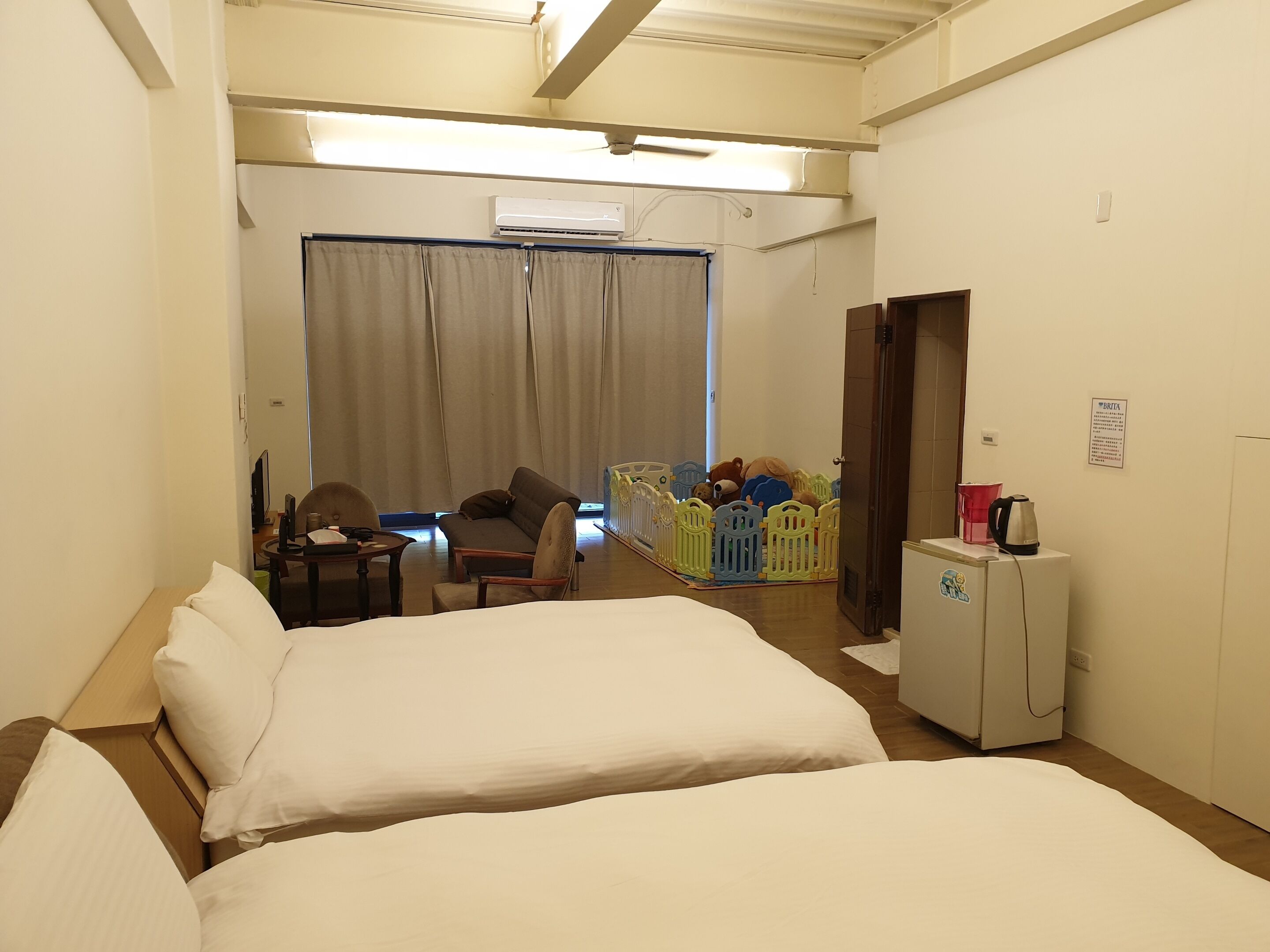 Habitación de hotel con dos camas, un escritorio con silla, una mesita, un refrigerador y una zona de juegos infantil con juguetes.