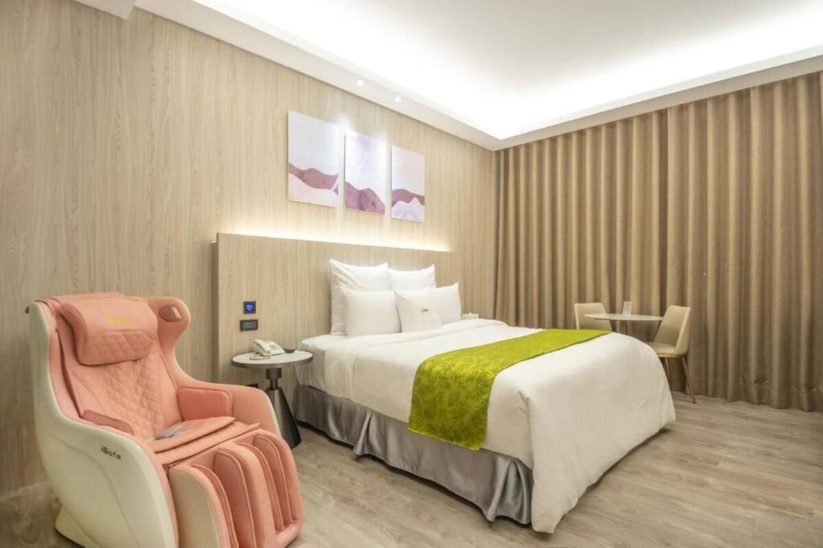A hotel room with a bed, a massage chair, a small table, and a curtain.