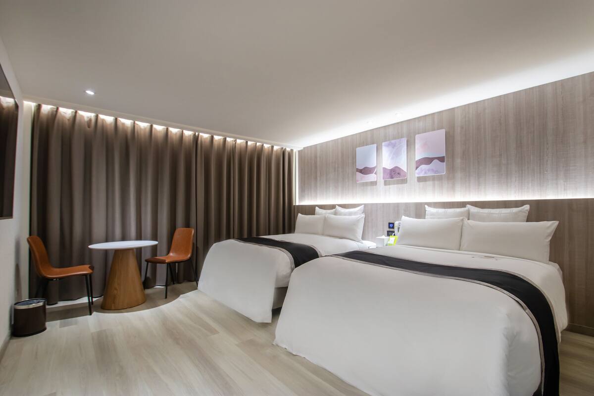 Una habitación de hotel con una cama grande, dos mesitas de noche, una mesita redonda pequeña y dos sillas.