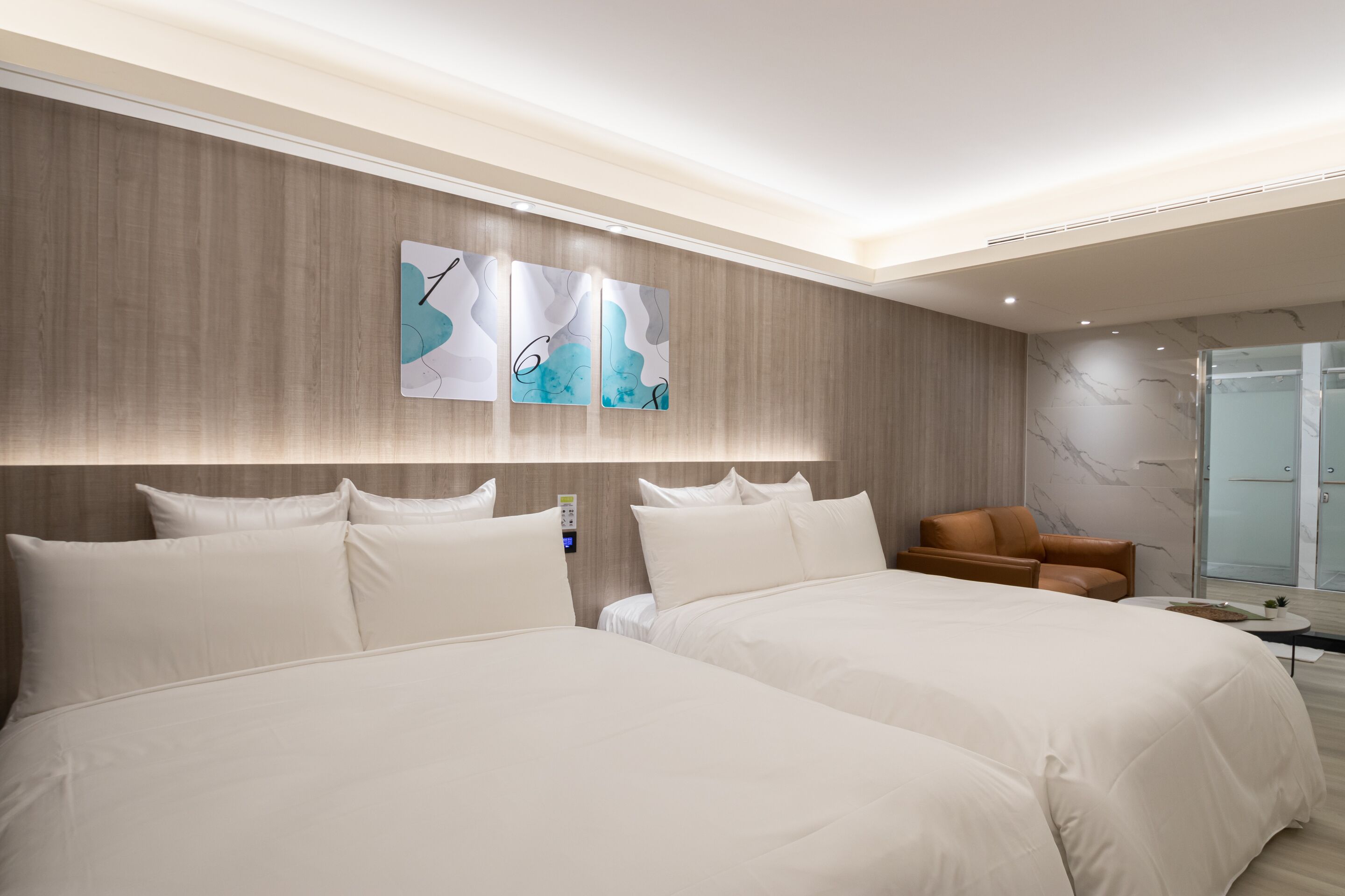 Una habitación de hotel moderna con dos camas grandes, un sillón de cuero marrón y arte abstracto en la pared.