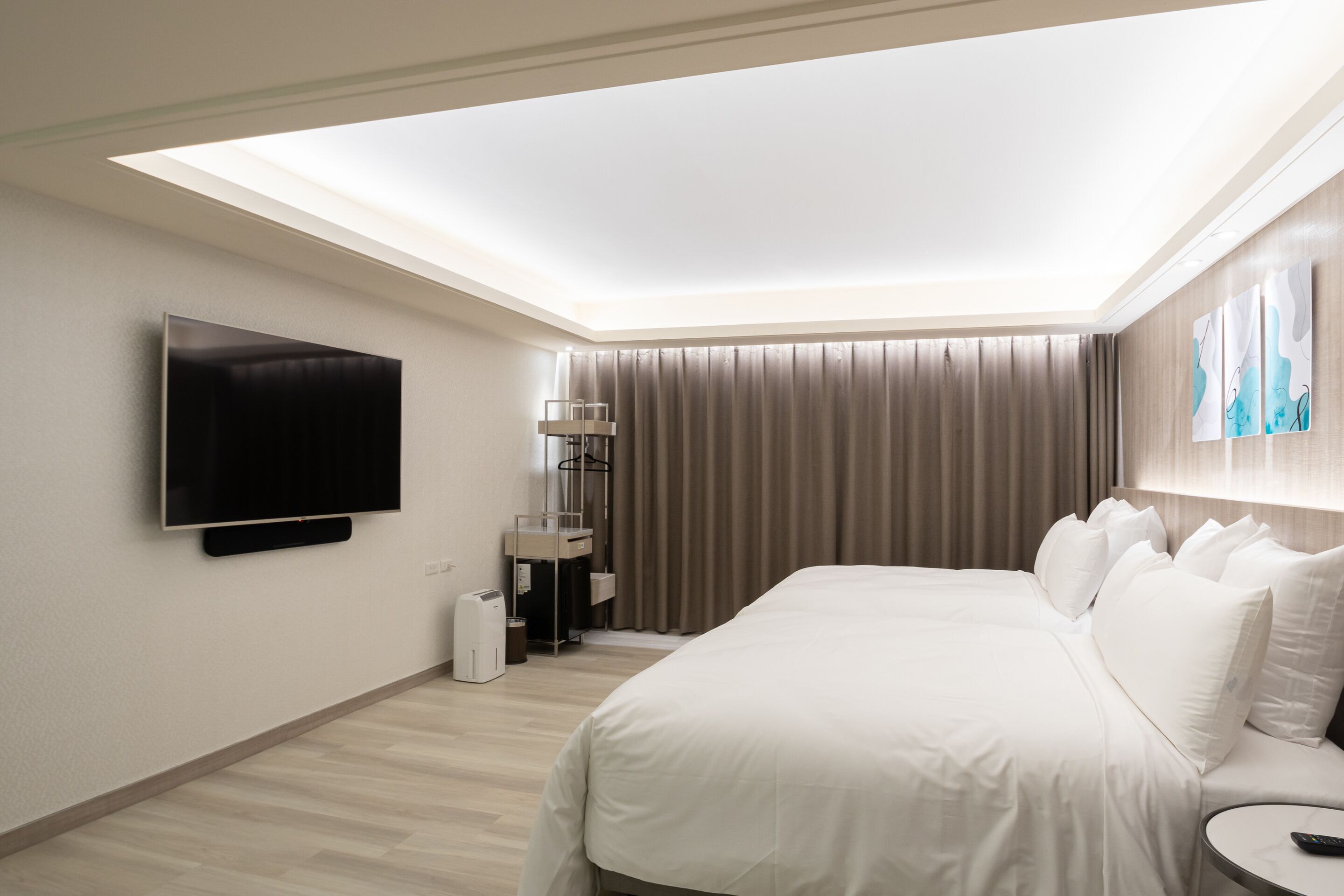 A modern hotel room with a large bed, a flat-screen TV mounted on the wall, a bedside table, and a ceiling skylight.