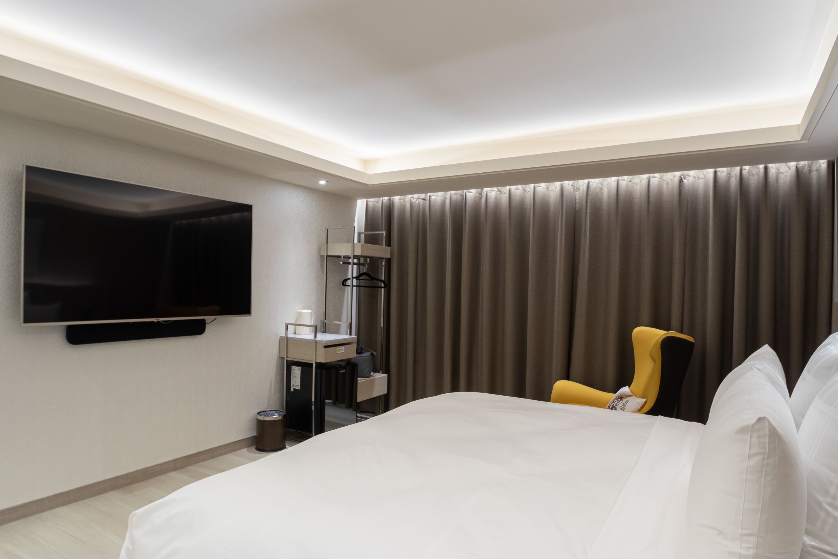 Una habitación de hotel moderna con una cama grande, un televisor de pantalla plana en la pared, un escritorio con una silla y una ventana con cortinas.