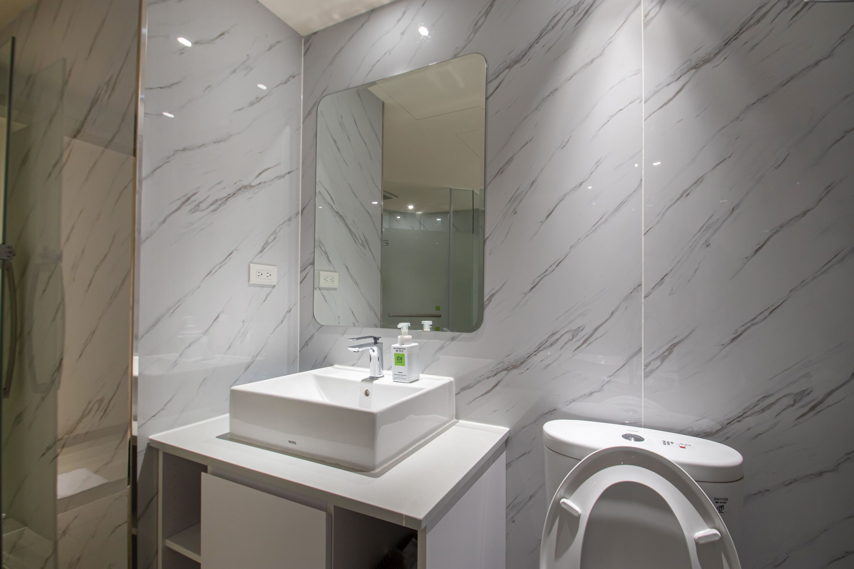 A modern bathroom with a marble backsplash, a white sink, a mirror, and a toilet.