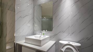 A modern bathroom with a marble backsplash, a white sink, a mirror, and a toilet.