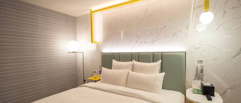 A modern hotel room with a neatly made bed, a bedside table with a lamp, and a wall-mounted phone.