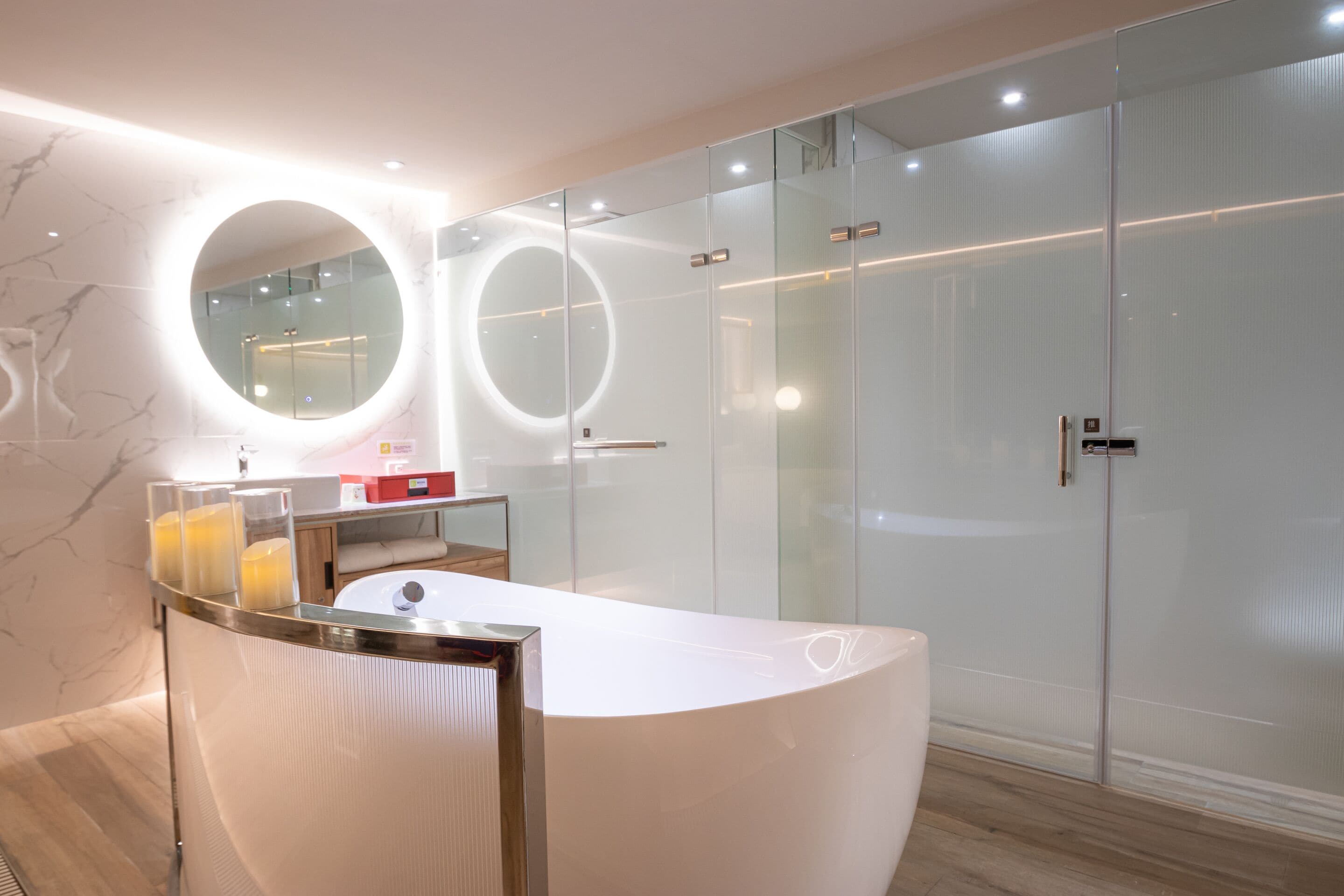 A modern bathroom with a curved white vanity, a round mirror, and a glass shower enclosure.