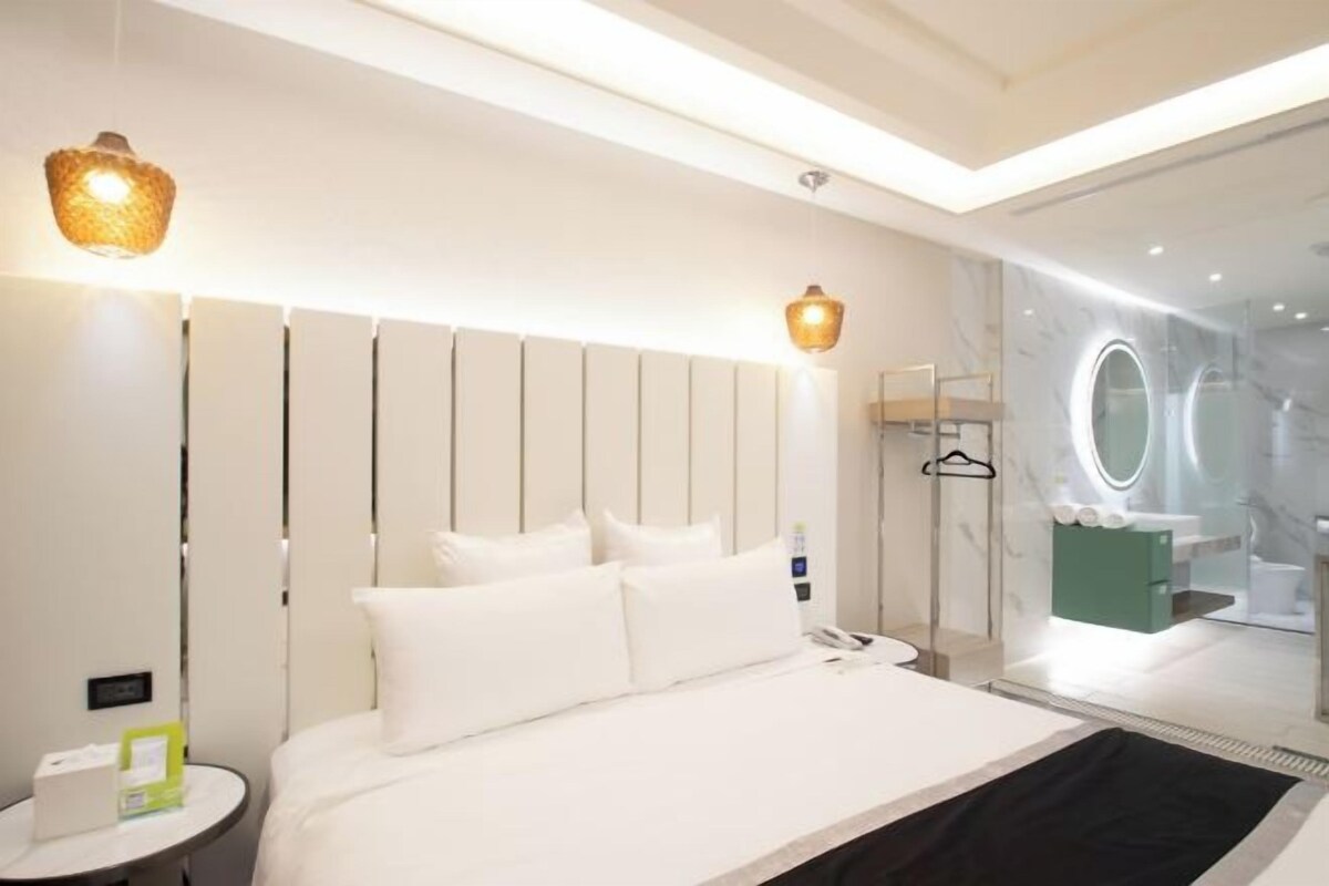 A modern hotel room with a large bed, bedside tables, a glass shower enclosure, and a view of the bathroom.