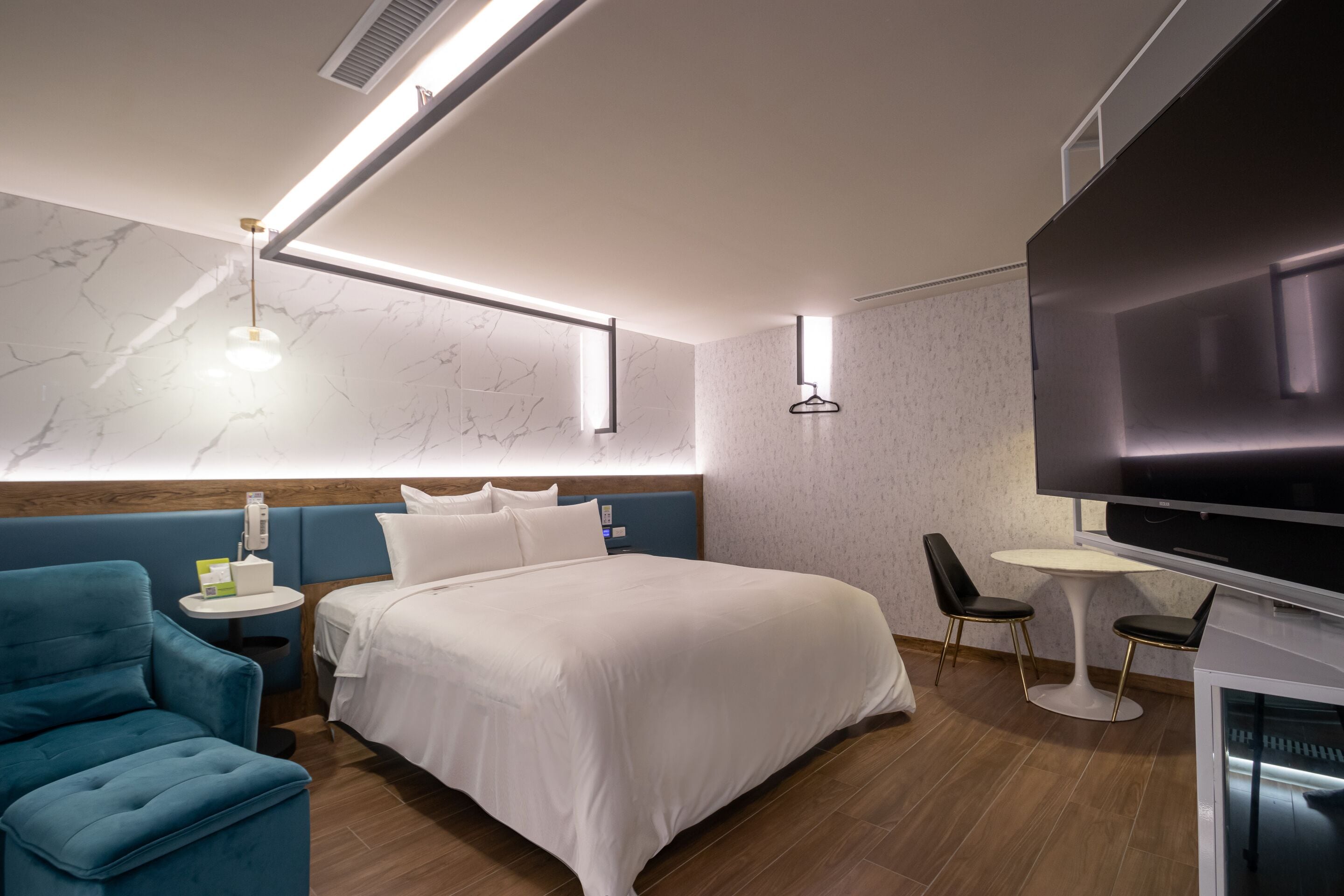 Habitación de hotel moderna con una cama grande, un televisor de pantalla plana, una mesita redonda y un sillón azul.