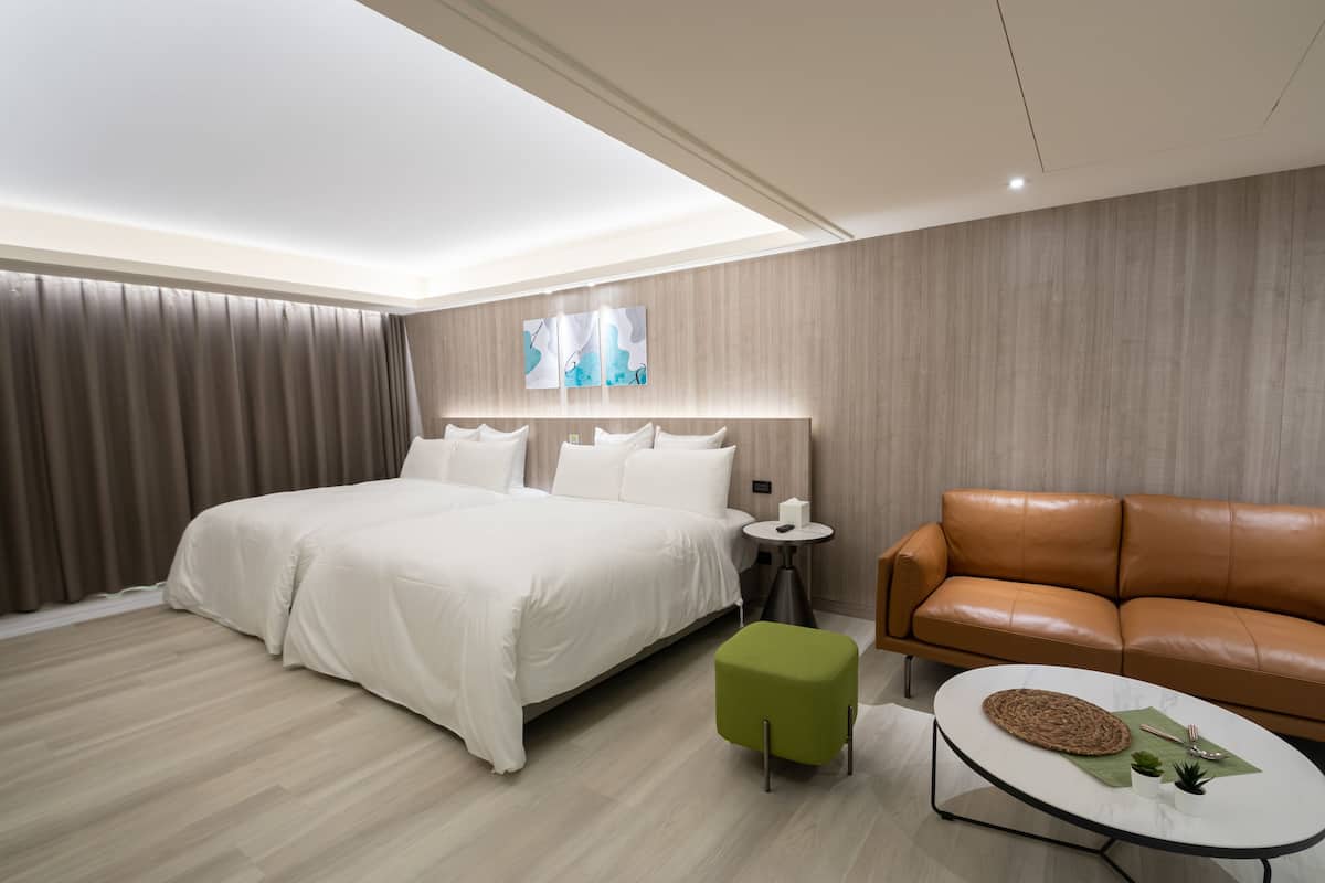 Una habitación de hotel moderna con una cama grande, un reposapiés verde, un sofá de cuero marrón y una pequeña mesa de centro.