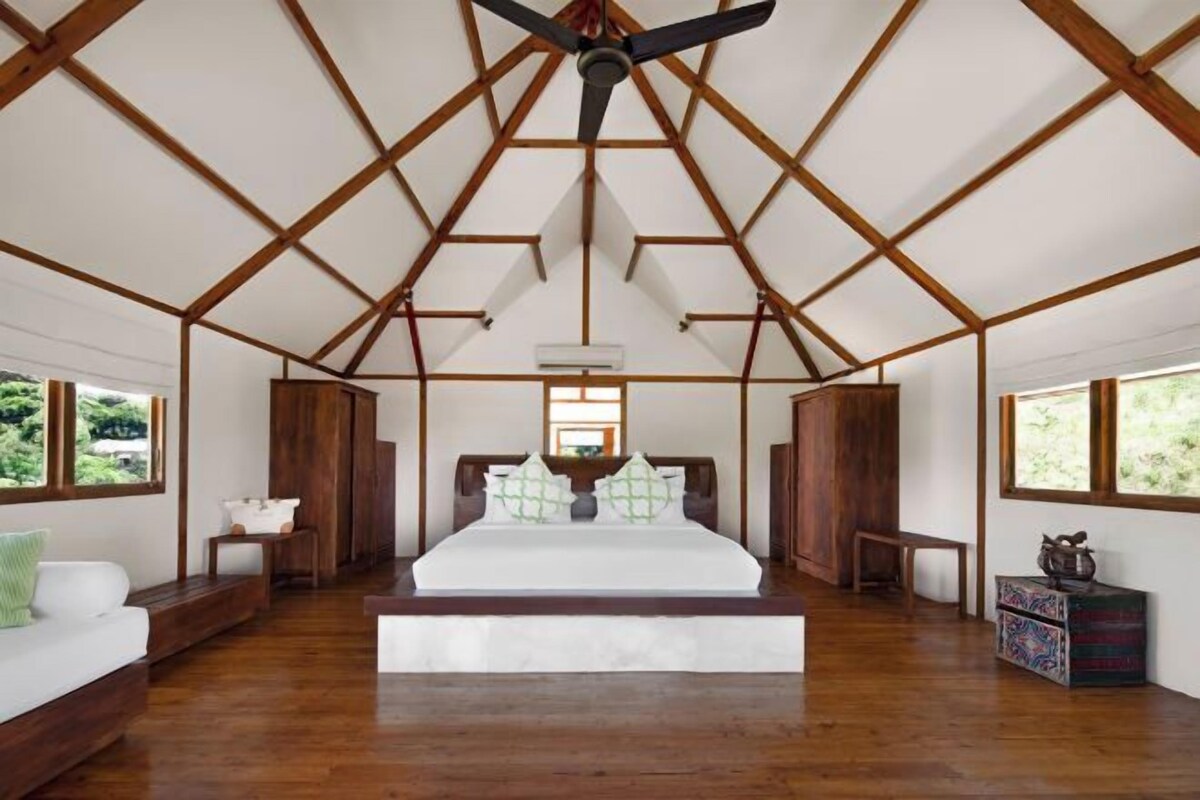 A spacious bedroom with a large bed, wooden beams, and a ceiling fan.