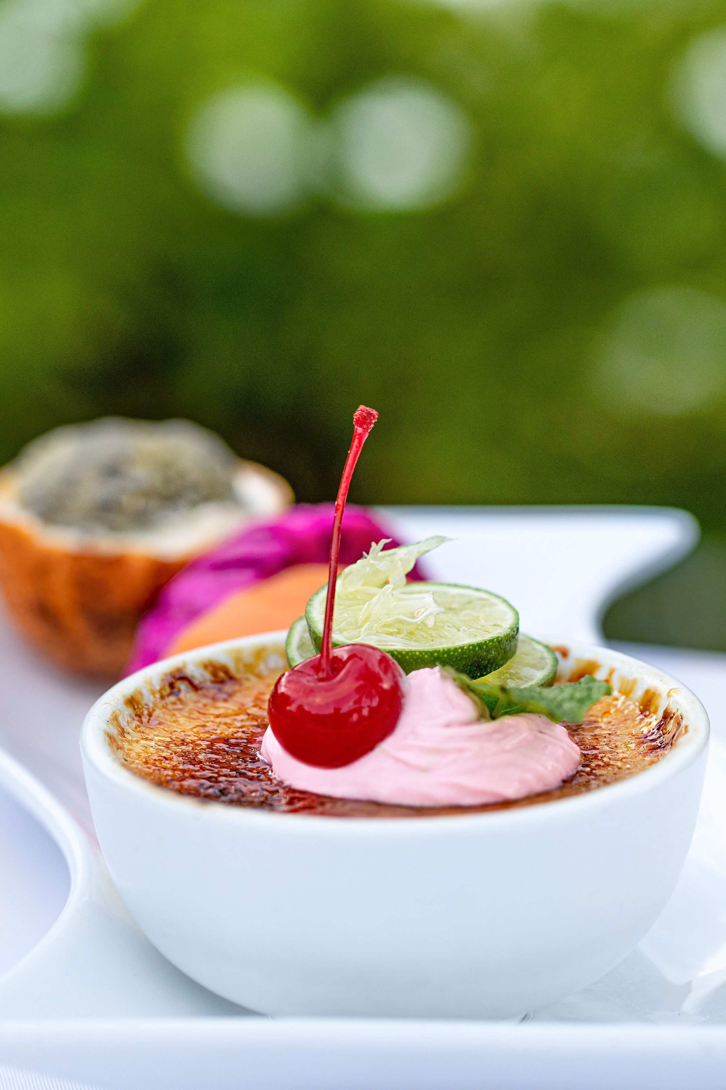 A dessert with a cherry on top, surrounded by lime slices and a half coconut shell.