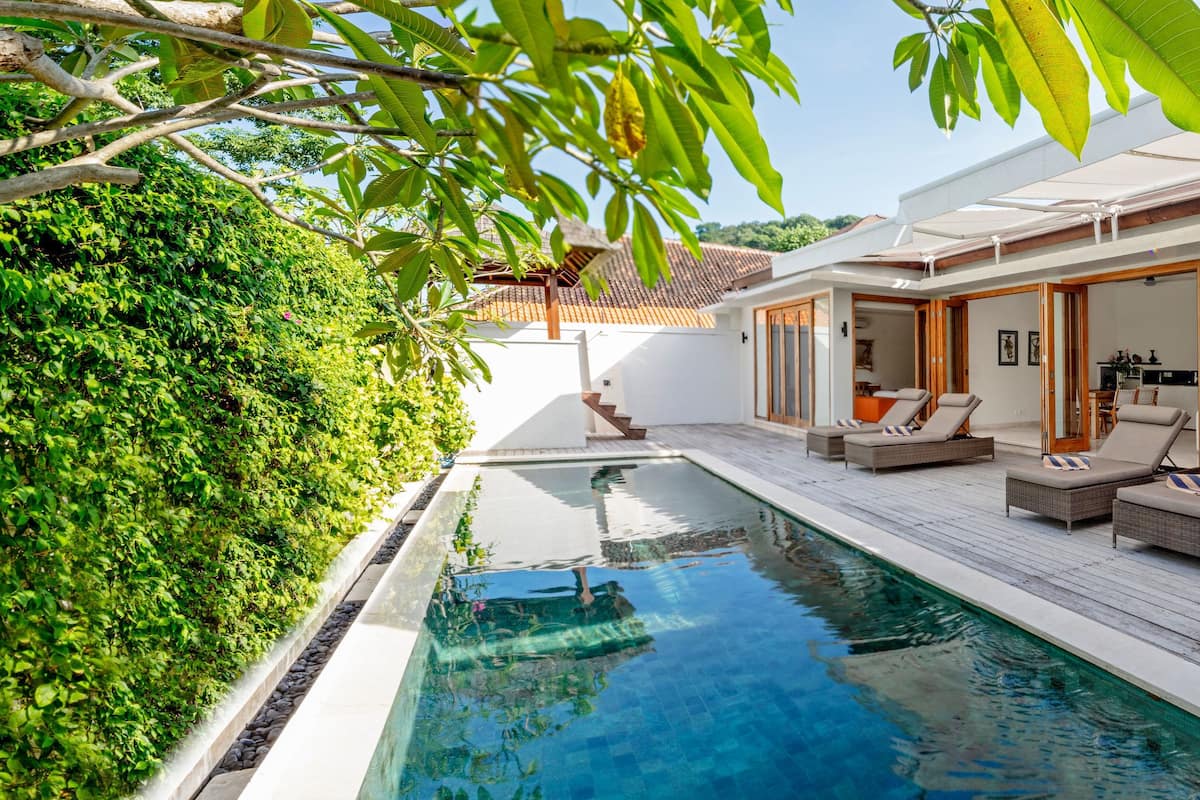 A modern pool area with a wooden deck, lounge chairs, and a lush green hedge.