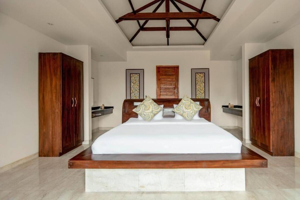 A bedroom with a large bed, wooden headboard, two wardrobes, and a ceiling with wooden beams.