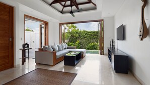A modern living room with a sofa, coffee table, and a TV mounted on the wall. - Kokomo Resort Gili Gede (Gili Gede)