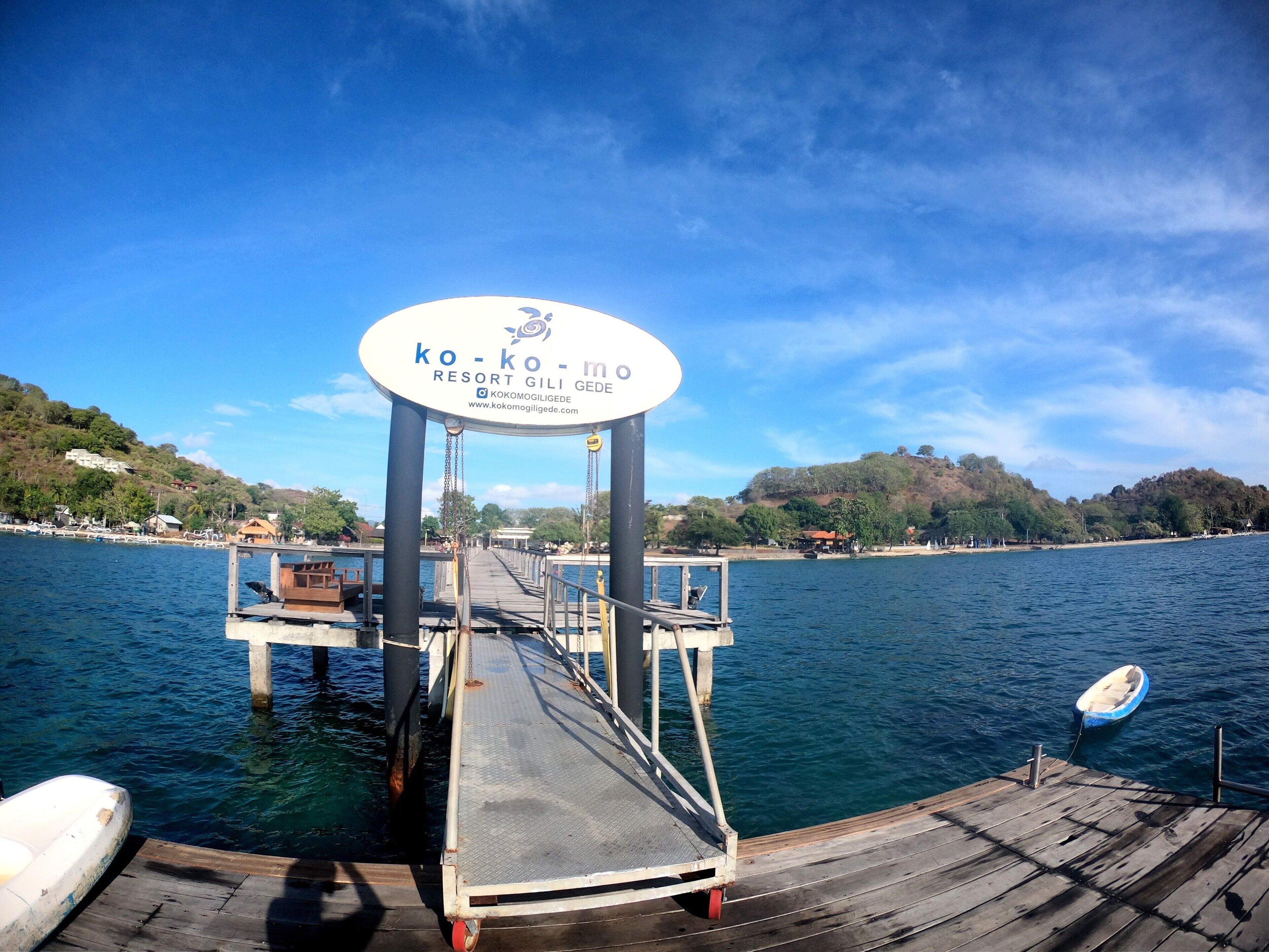 A wooden pier leading to a sign for Kokomo Resort Gili Gede.