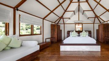 Een slaapkamer met een houten plafond, een groot bed, een bank en een raam met uitzicht op groen.