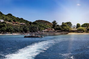 A pier extending into a body of water with a boat moving away, surrounded by hills and buildings. - Kokomo Resort Gili Gede (Gili Gede)