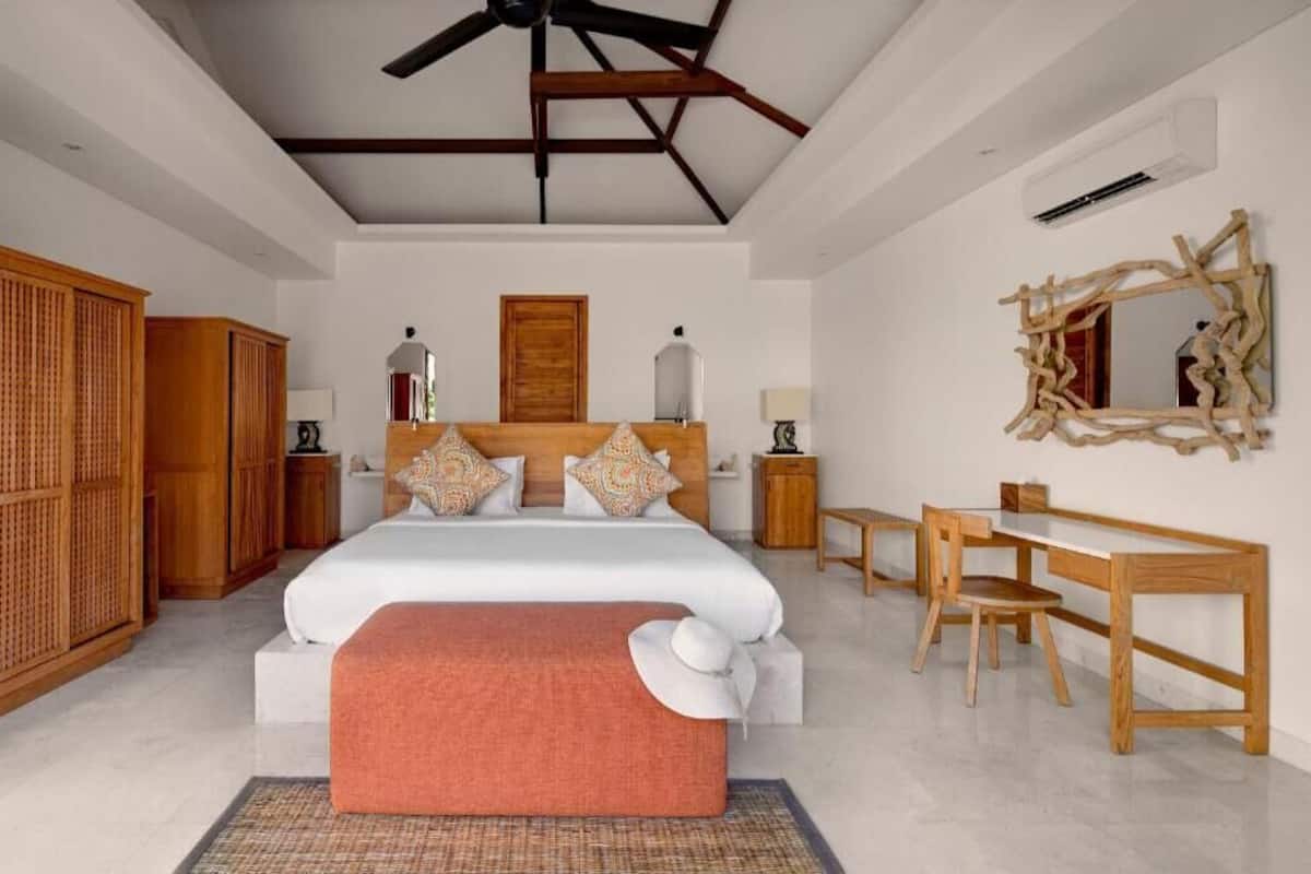 A bedroom with a large bed, wooden furniture, a desk, and a mirror.