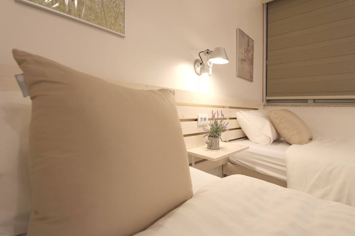Ein Hotelzimmer mit zwei Betten, einem Nachttisch mit Lampe, einer kleinen Topfpflanze und einem Bild an der Wand.
