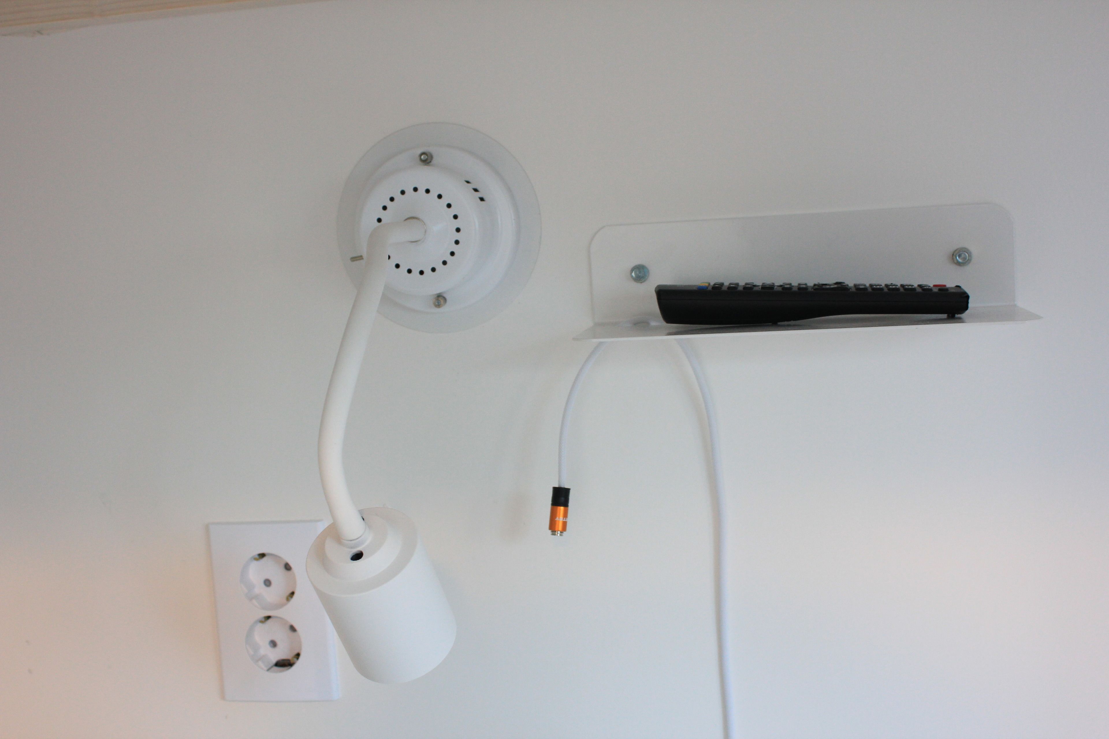 A wall-mounted electrical outlet with a white cord and a black remote control on a clear shelf.