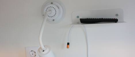 A wall-mounted electrical outlet with a white cord and a black remote control on a clear shelf.