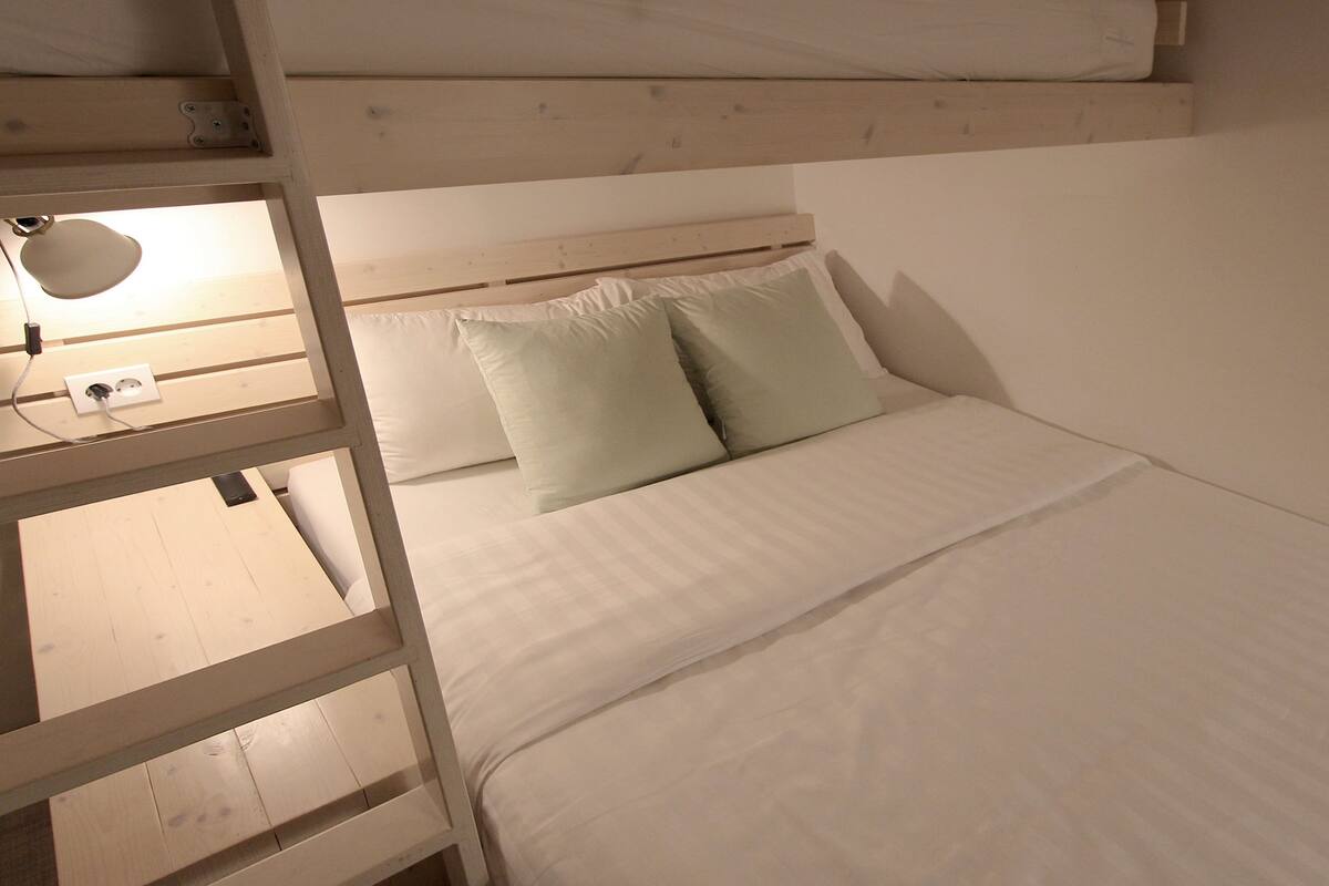 Ein Stockbett mit Holzkopfteil, ein Nachttisch mit Lampe und eine weiße Matratze mit zwei Kissen.