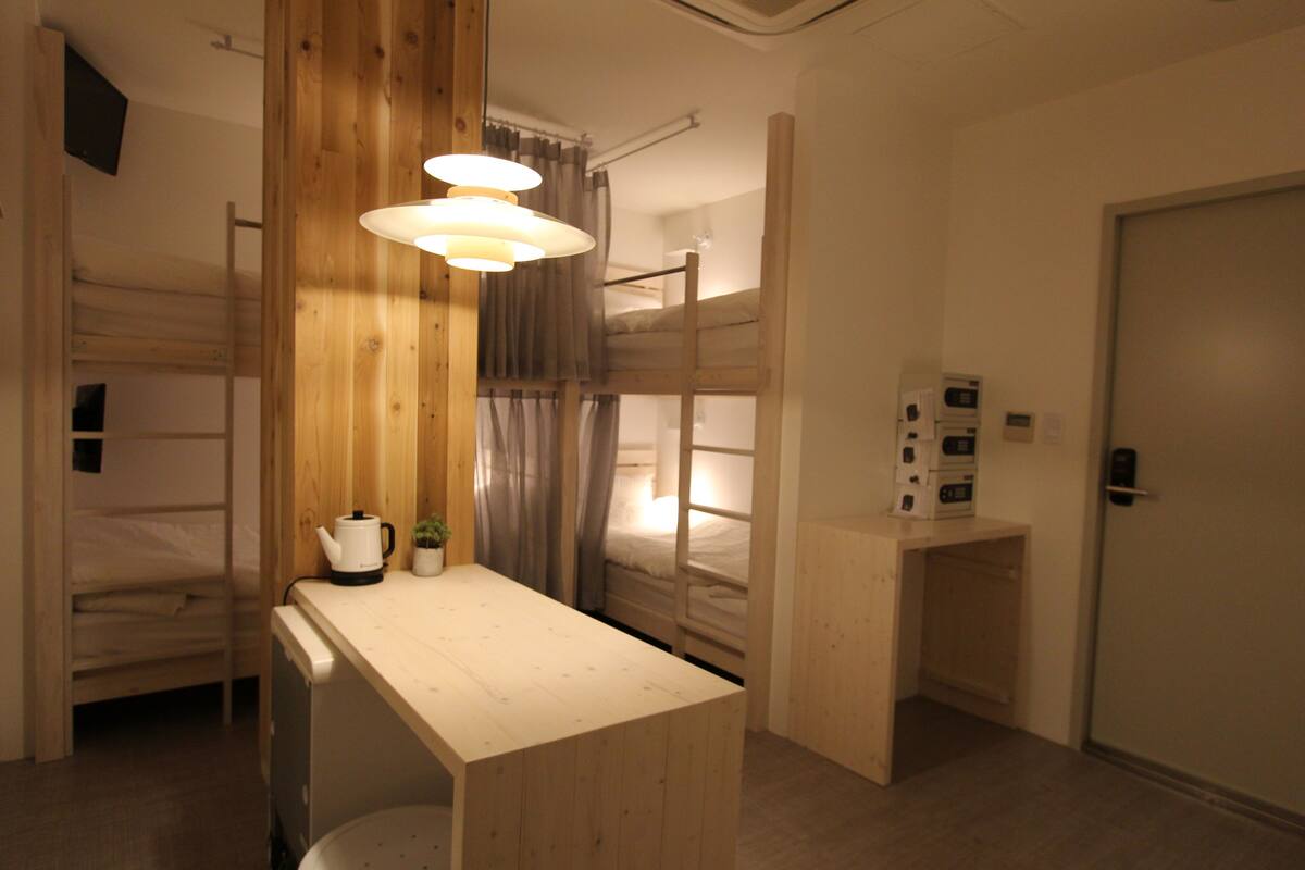 Ein Zimmer mit Etagenbetten, einem Holztisch, einem Wasserkocher und einer kleinen Pflanze.