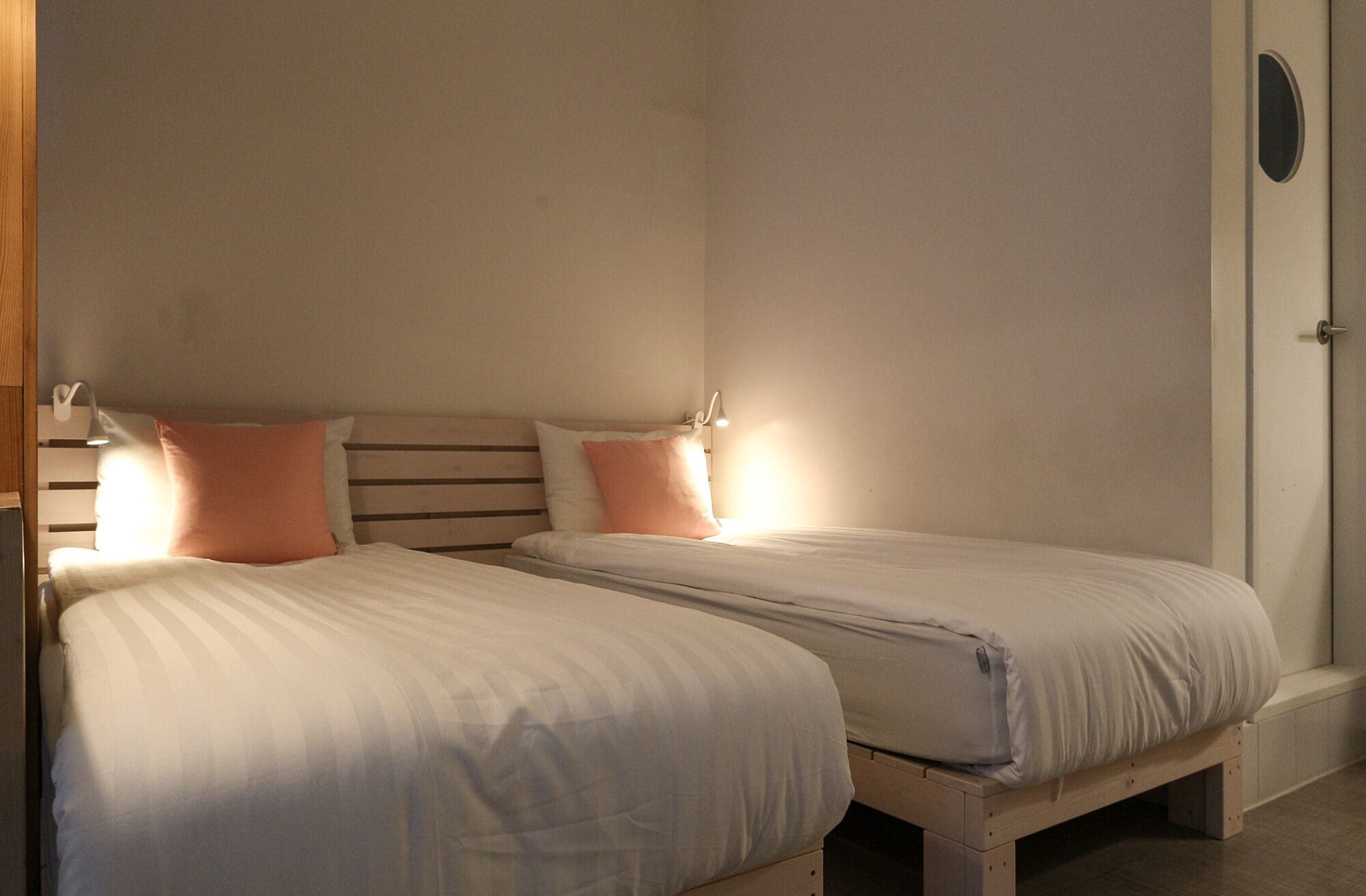 A room with two single beds, each with a headboard, bedside lamps, and a door on the right.