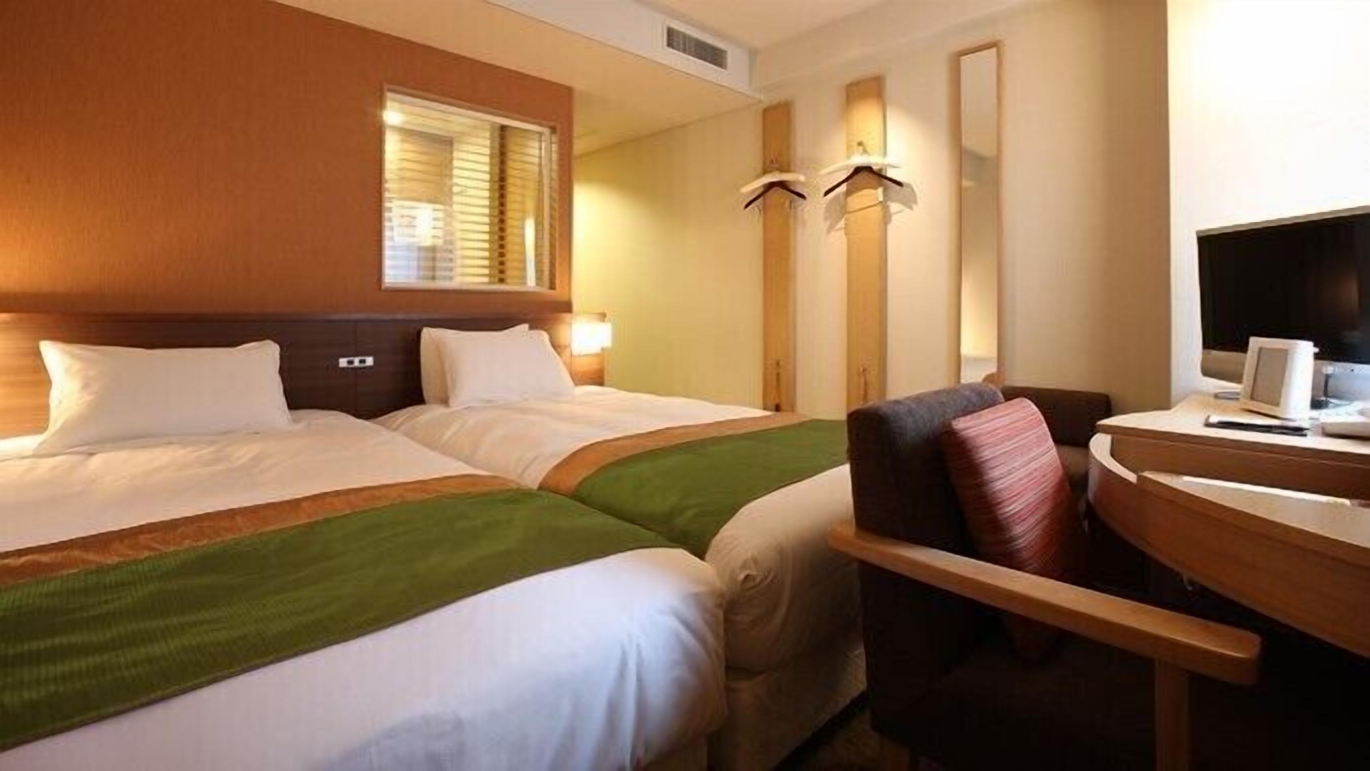 Una habitación de hotel con dos camas, un escritorio con una computadora y una silla.