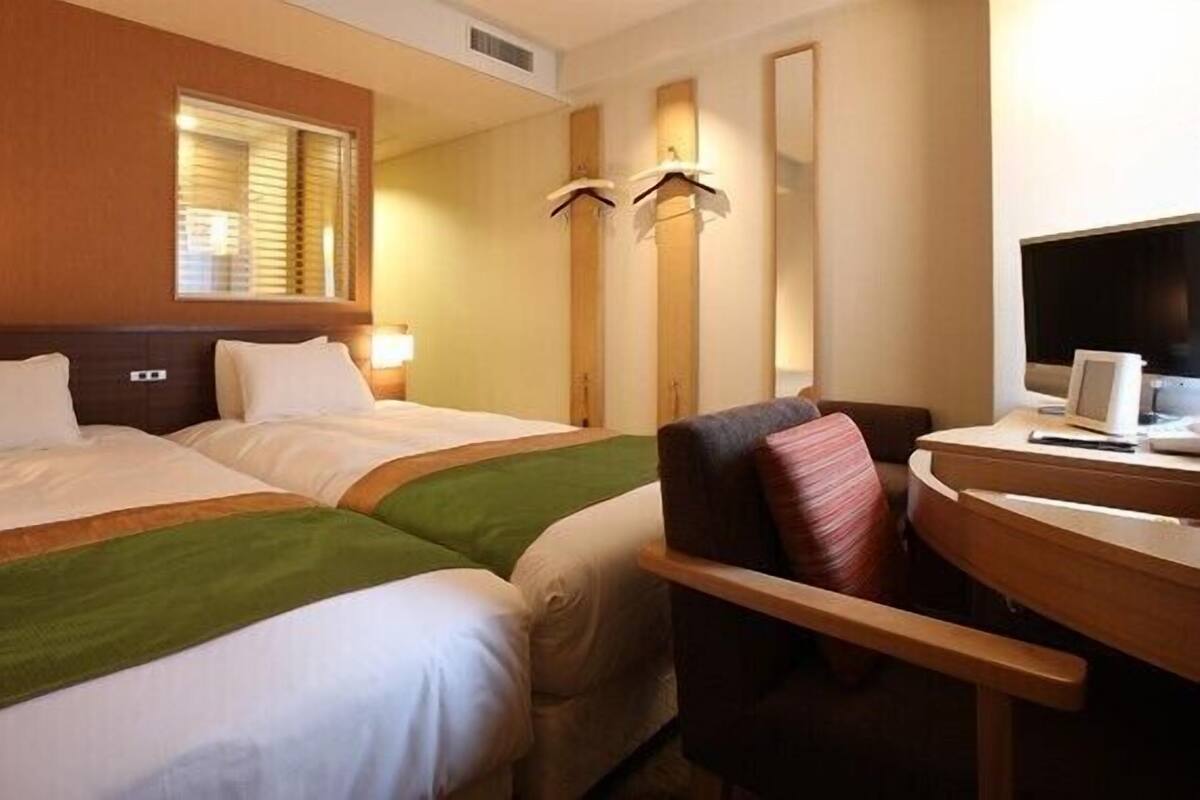 Une chambre d’hôtel avec deux lits, un bureau avec un ordinateur et une chaise.