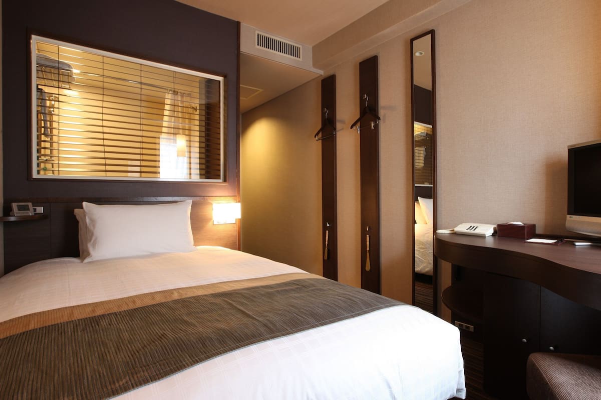 Une chambre d’hôtel comprenant un lit, une lampe de chevet, un bureau avec une télévision et un miroir.
