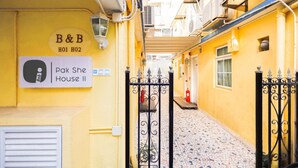 Ein schmaler Gang mit einem gelben Gebäude, einem Schild für 'Pak She House II' und einem schwarzen schmiedeeisernen Tor.
