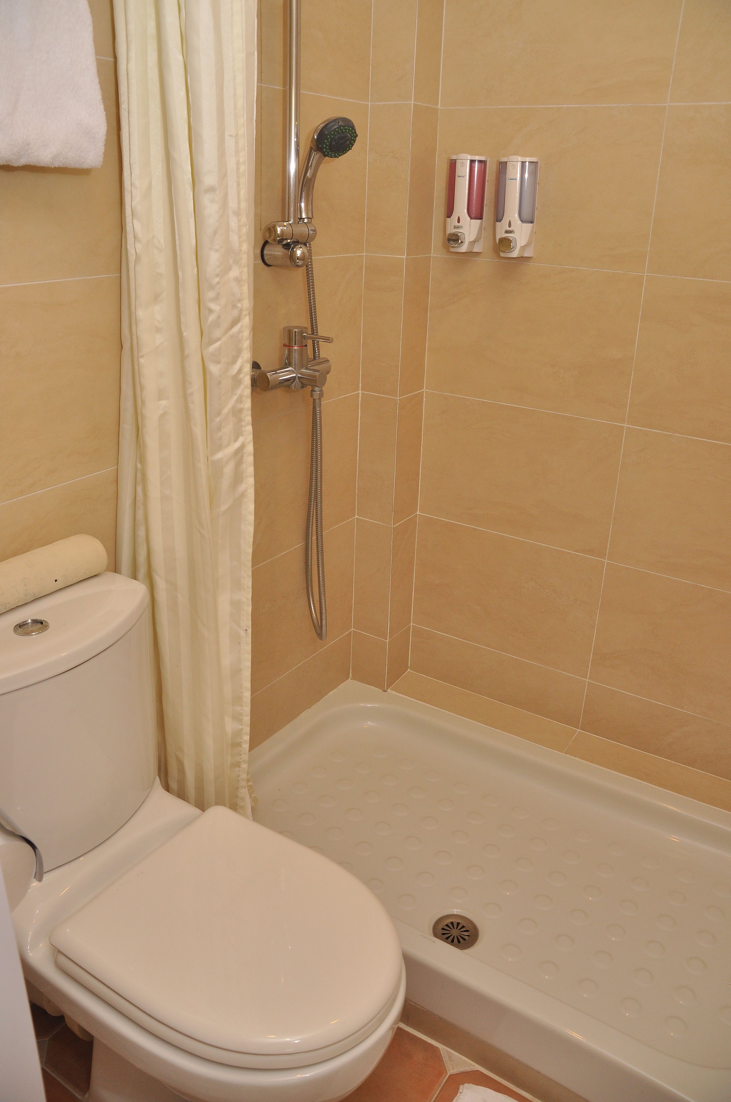 A bathroom with a toilet, shower, and two soap dispensers on the wall.