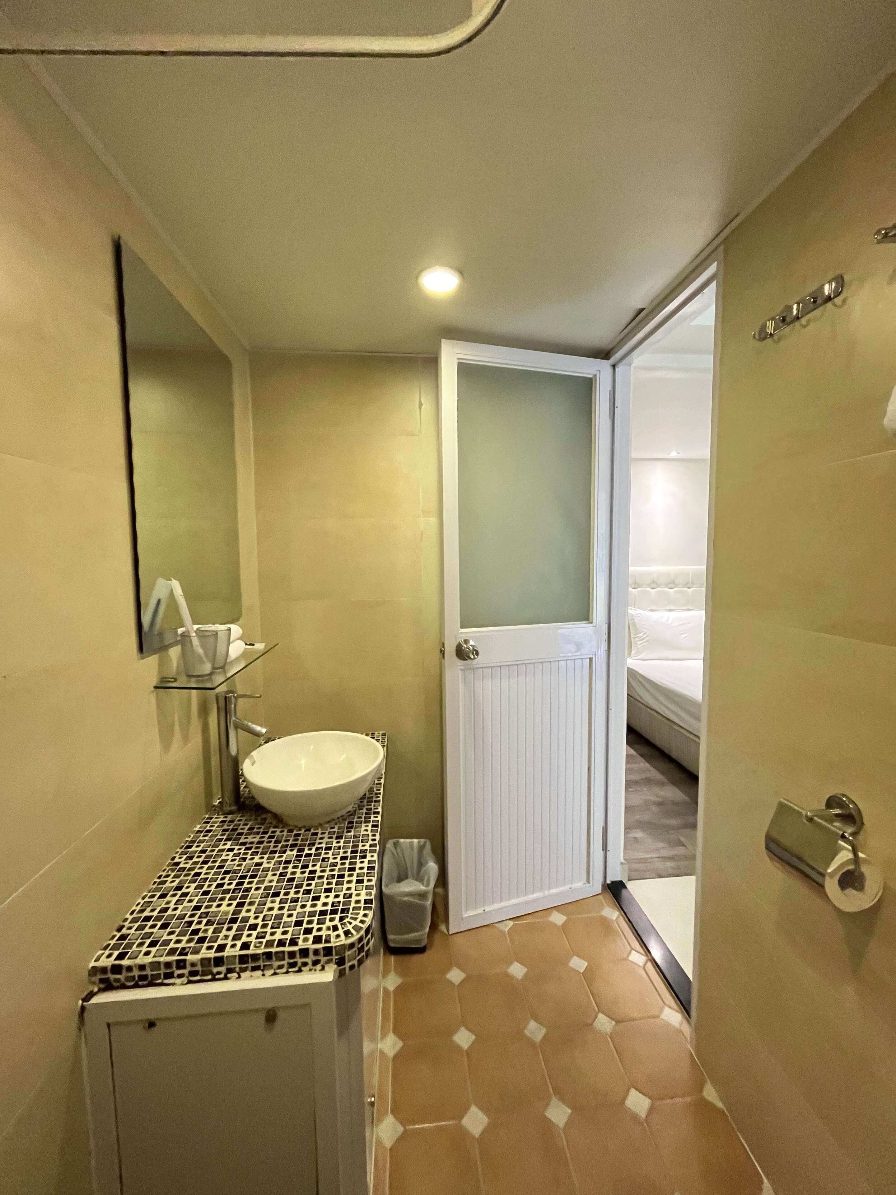 A compact bathroom with a white sink, a mirror, and a small trash bin.