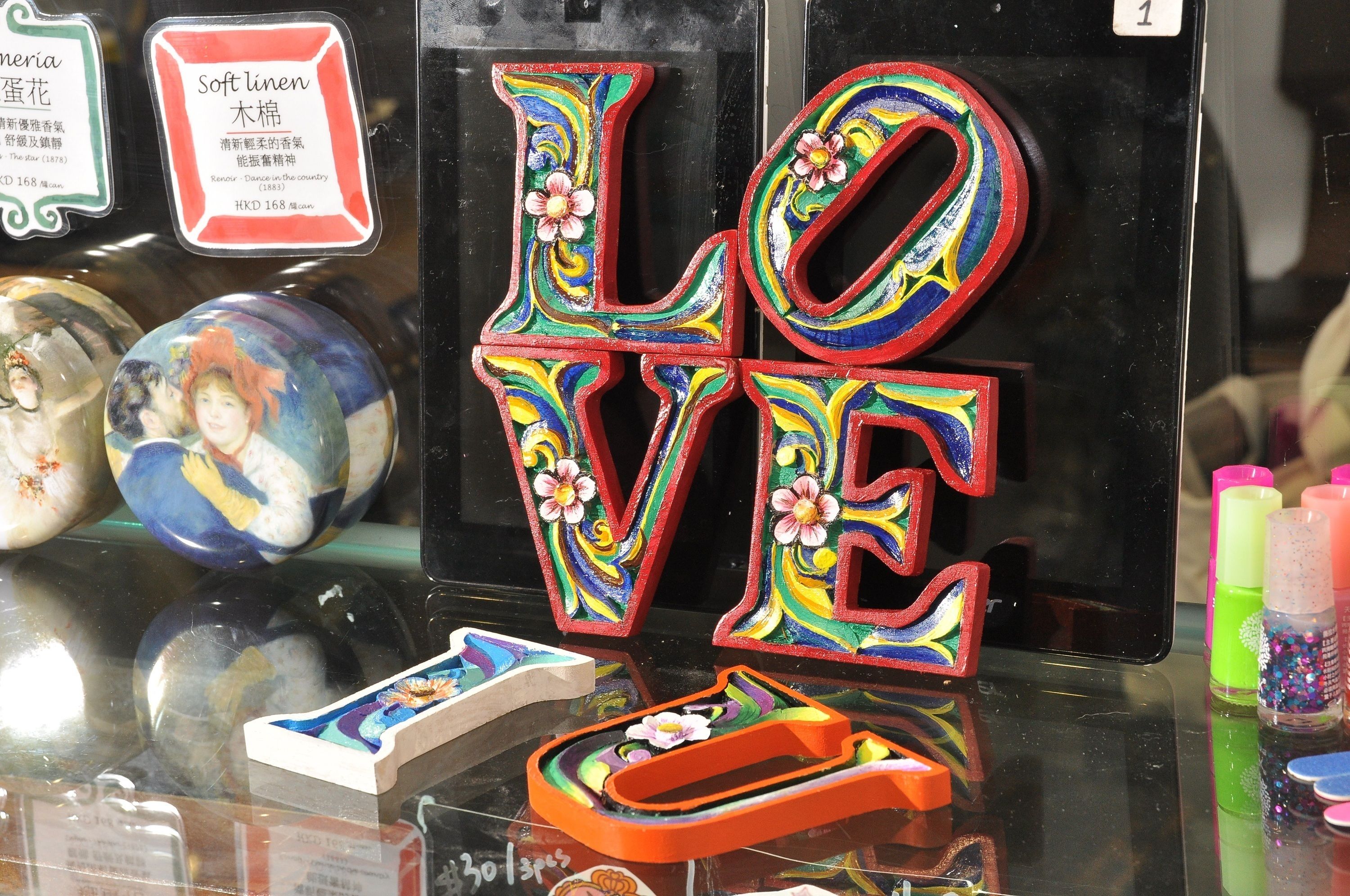 A display of colorful, floral-patterned letters spelling "LOVE" on a reflective surface, surrounded by various decorative items.