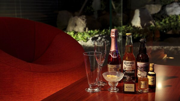 Une table en bois sur laquelle se trouvent diverses bouteilles et différents verres, notamment une bouteille de Corona Extra, une bouteille de Hibiki et une bouteille de Royal.