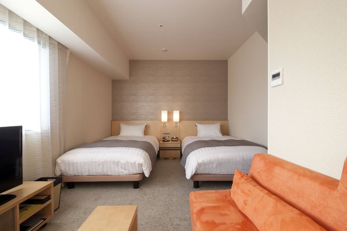 A hotel room with two beds, a TV, a sofa, and a small table.