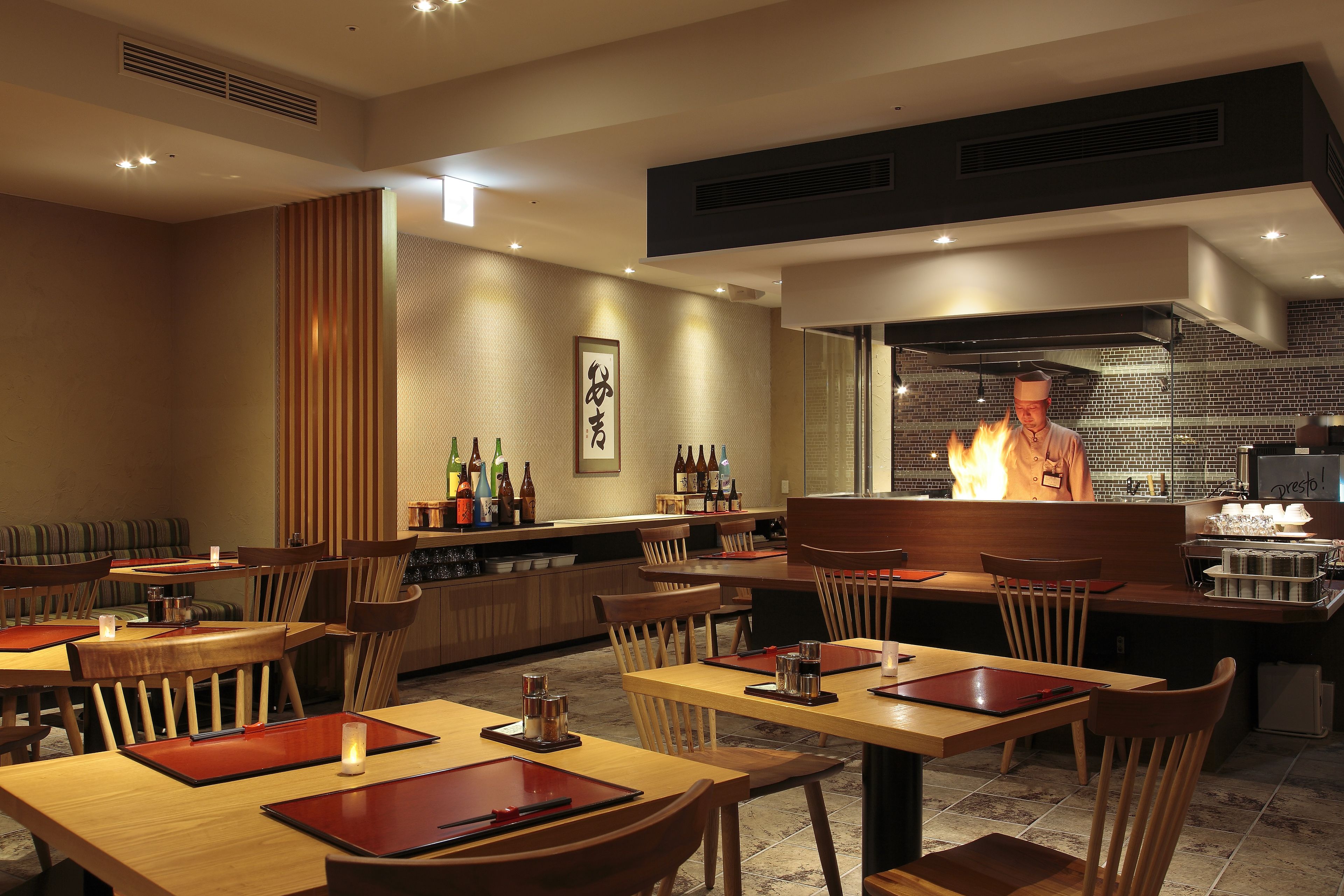 A restaurant with wooden tables and chairs, a bar area, and a chef preparing food.