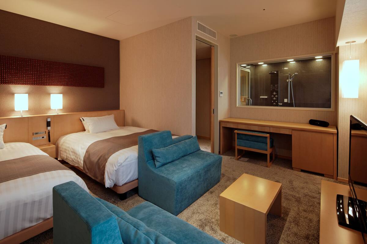 A hotel room with two beds, a desk, a chair, and a sofa.